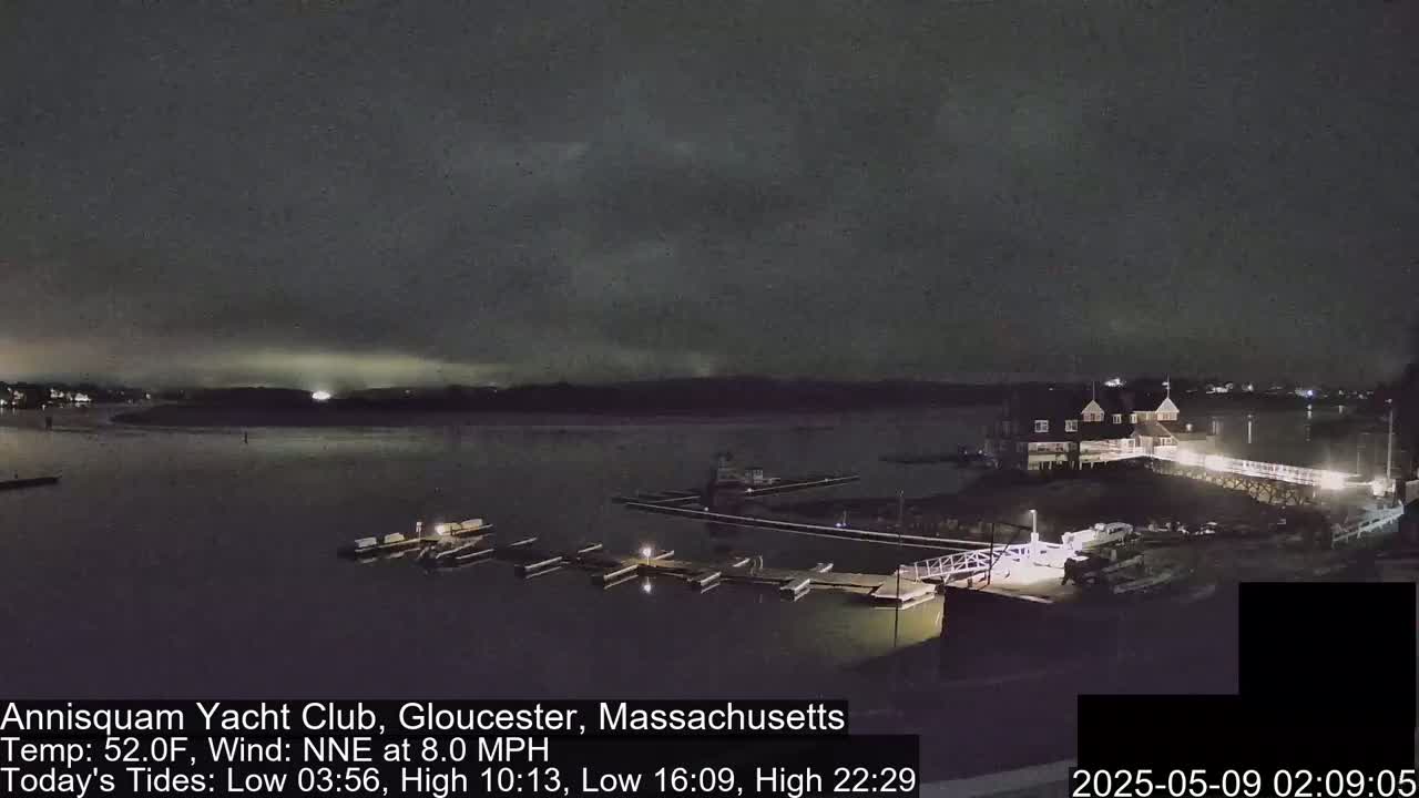 A nighttime view of a marina with boats docked, under a mostly cloudy sky.
