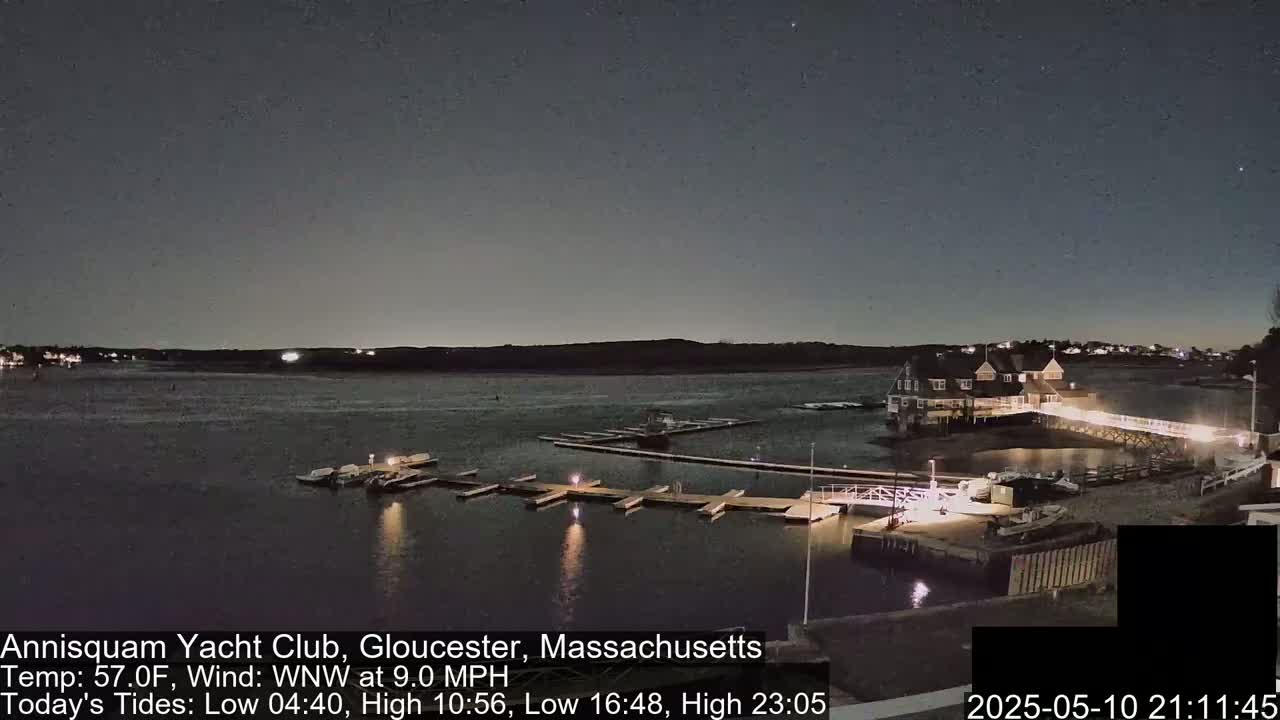 A nighttime view of a calm body of water with boats docked at a marina next to a lit building under a dark, clear sky.