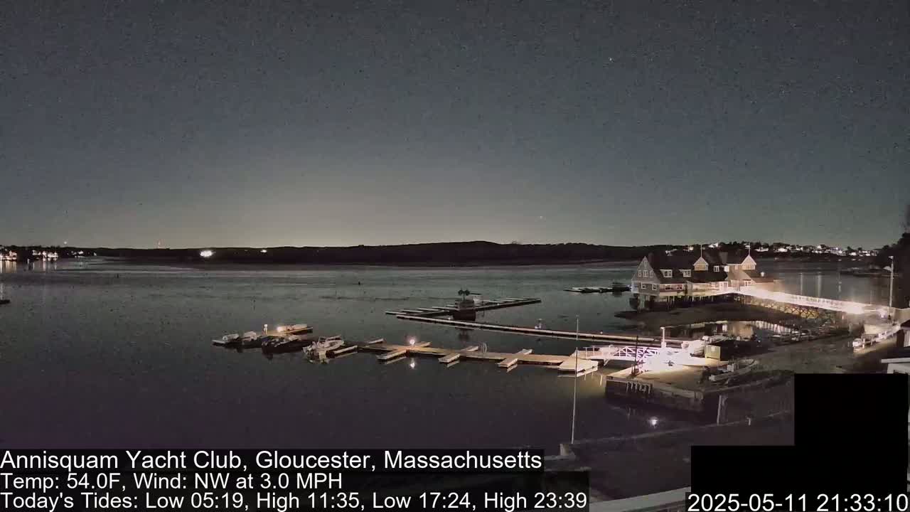 A nighttime view of a yacht club on a calm body of water under a dark sky.