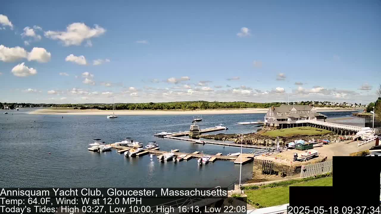 A marina filled with boats sits on a calm body of water under a partly cloudy sky.