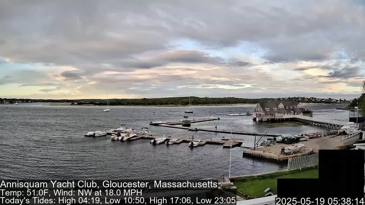 A calm body of water shows a marina with boats docked, a large clubhouse on the water, and a partly cloudy sky with a hint of sunset.