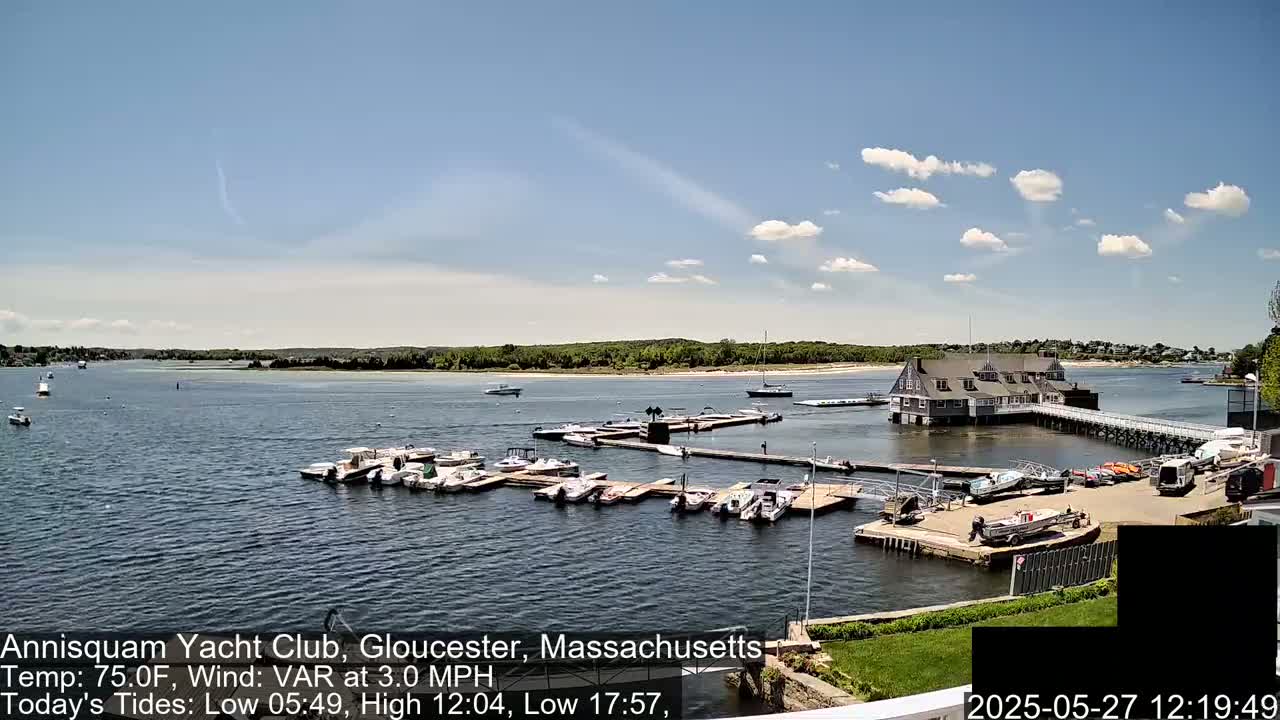 A marina filled with numerous boats is situated on a calm body of water under a partly cloudy sky.