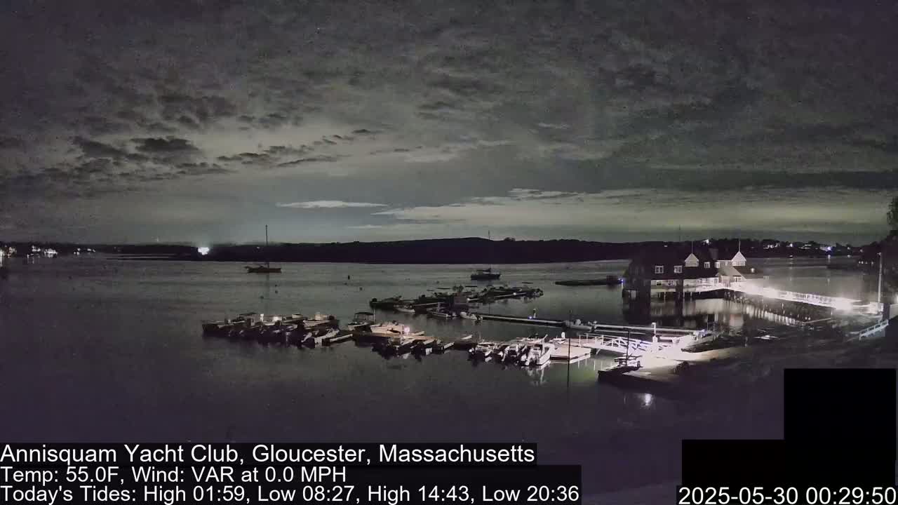 A nighttime view of a harbor with numerous boats moored at a marina under a cloudy sky.