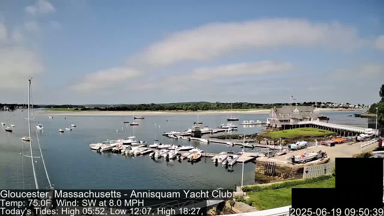 A marina filled with numerous boats is situated on a calm body of water under a partly cloudy sky.
