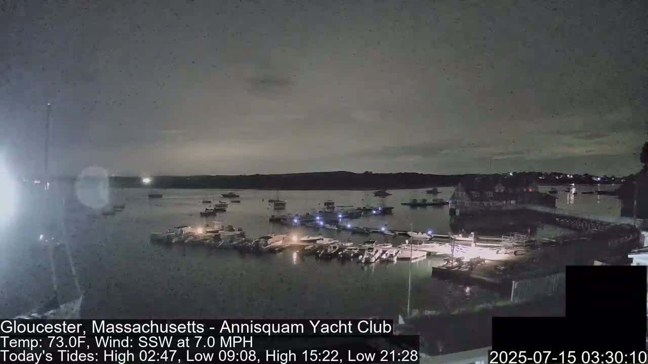 A nighttime view of a harbor filled with docked boats under a mostly cloudy sky.