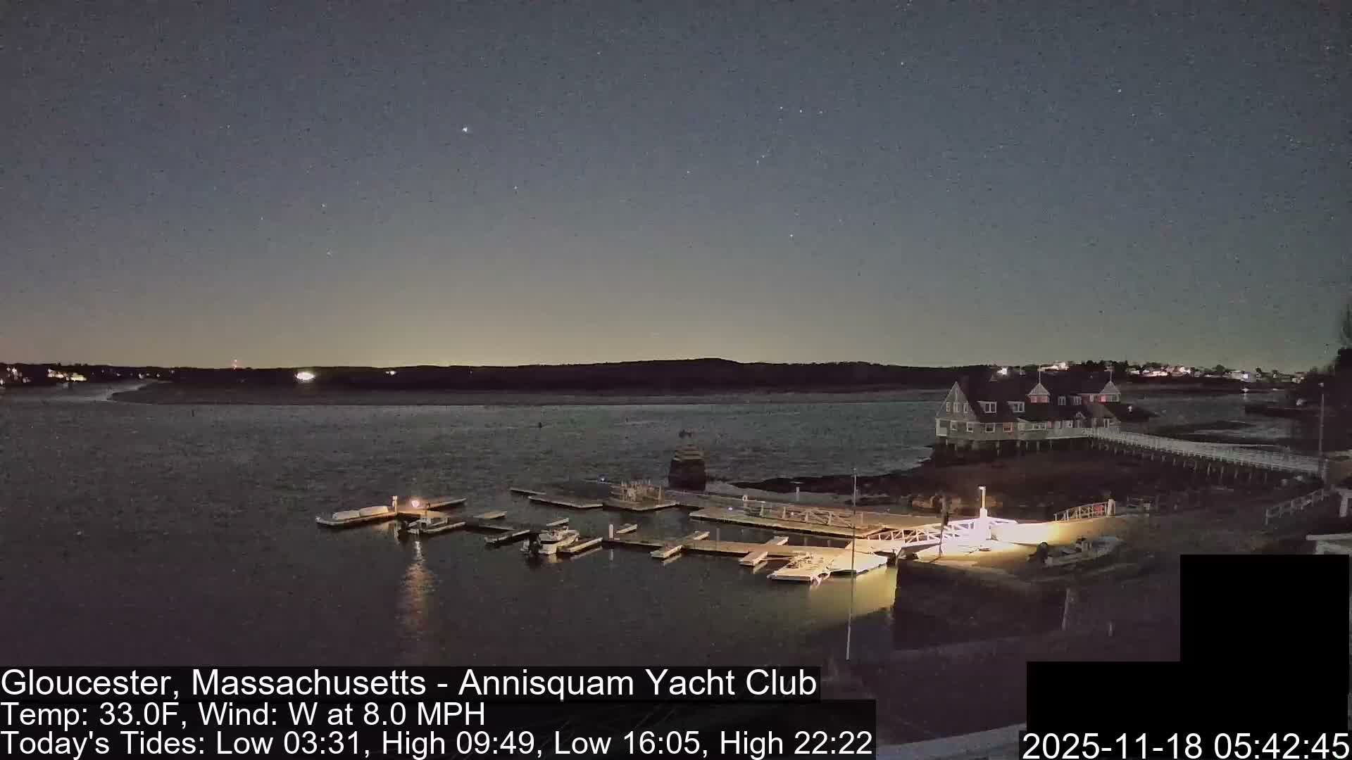 A nighttime view shows several boats moored in a dark harbor with distant shore lights, while prominent bright, irregular light patterns partially obscure the foreground.
