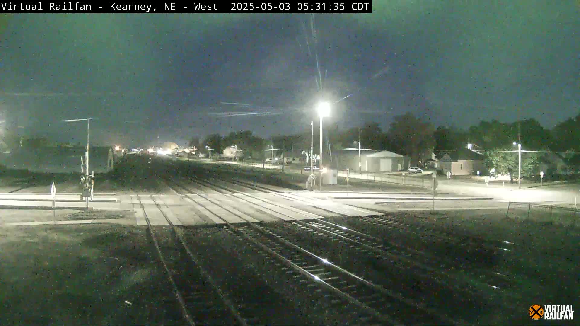 Under a dark night sky, railroad tracks intersect with a road at a crossing in a small town.