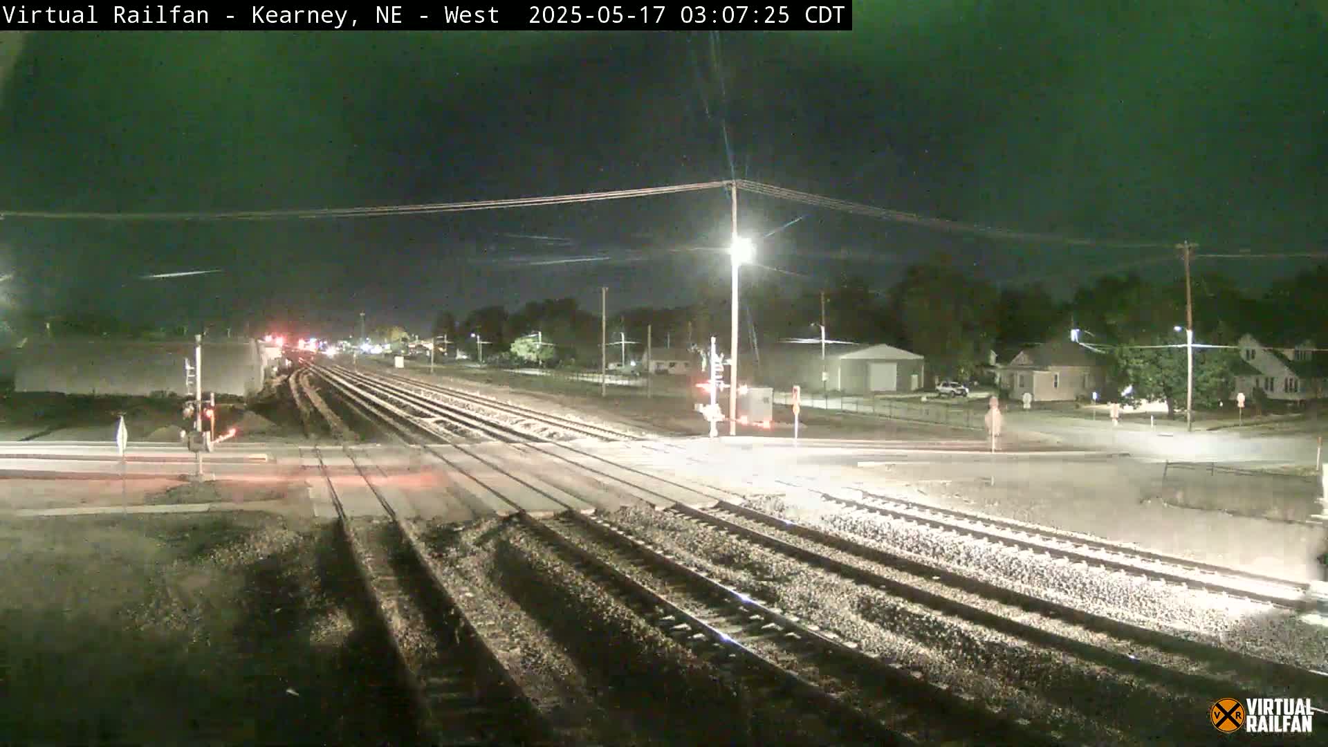 A nighttime view of a railroad crossing with several sets of tracks intersecting a road, under a clear, dark sky.