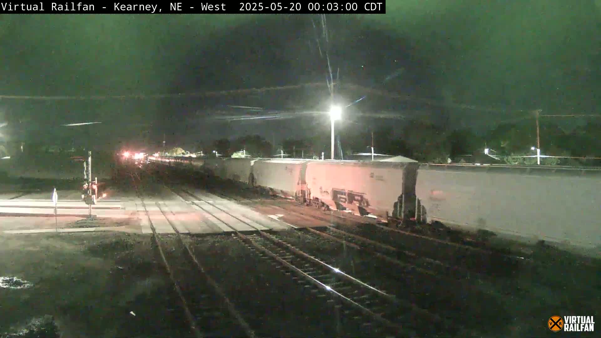 A long freight train, mostly composed of white boxcars, is slowly moving at night under a dark, clear sky, along railway tracks.
