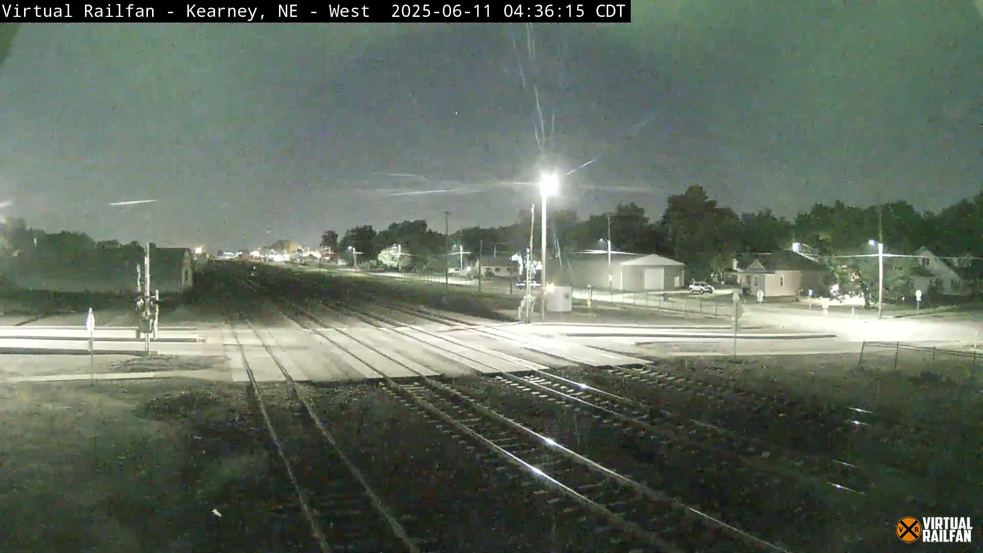 A nighttime view of a railway crossing in a residential area under a mostly clear sky.