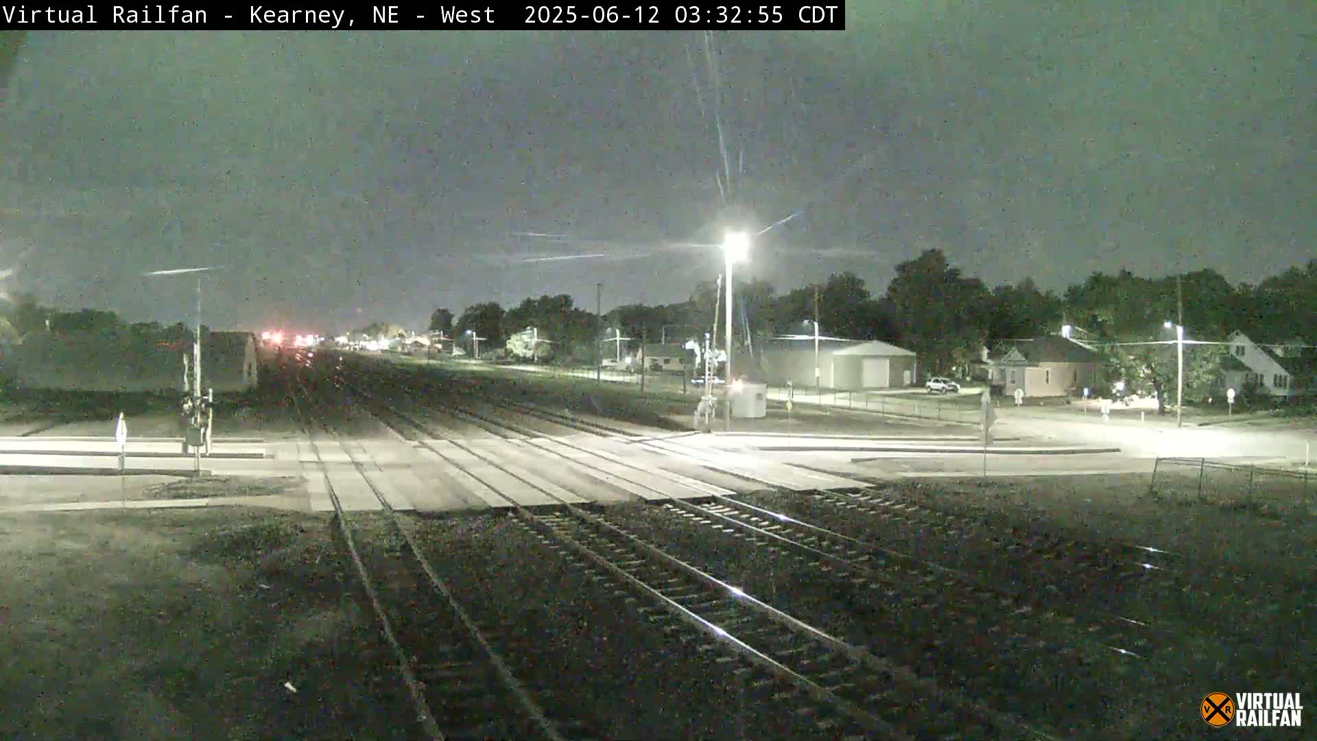 A nighttime view of a railroad crossing near a residential area under a mostly clear sky.