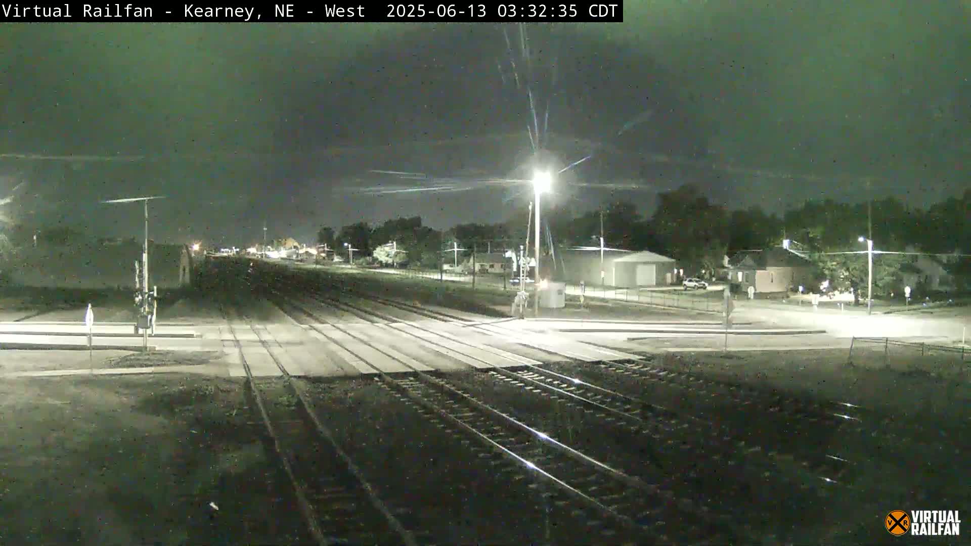 A nighttime view of a railroad crossing in a residential area under a dark sky.