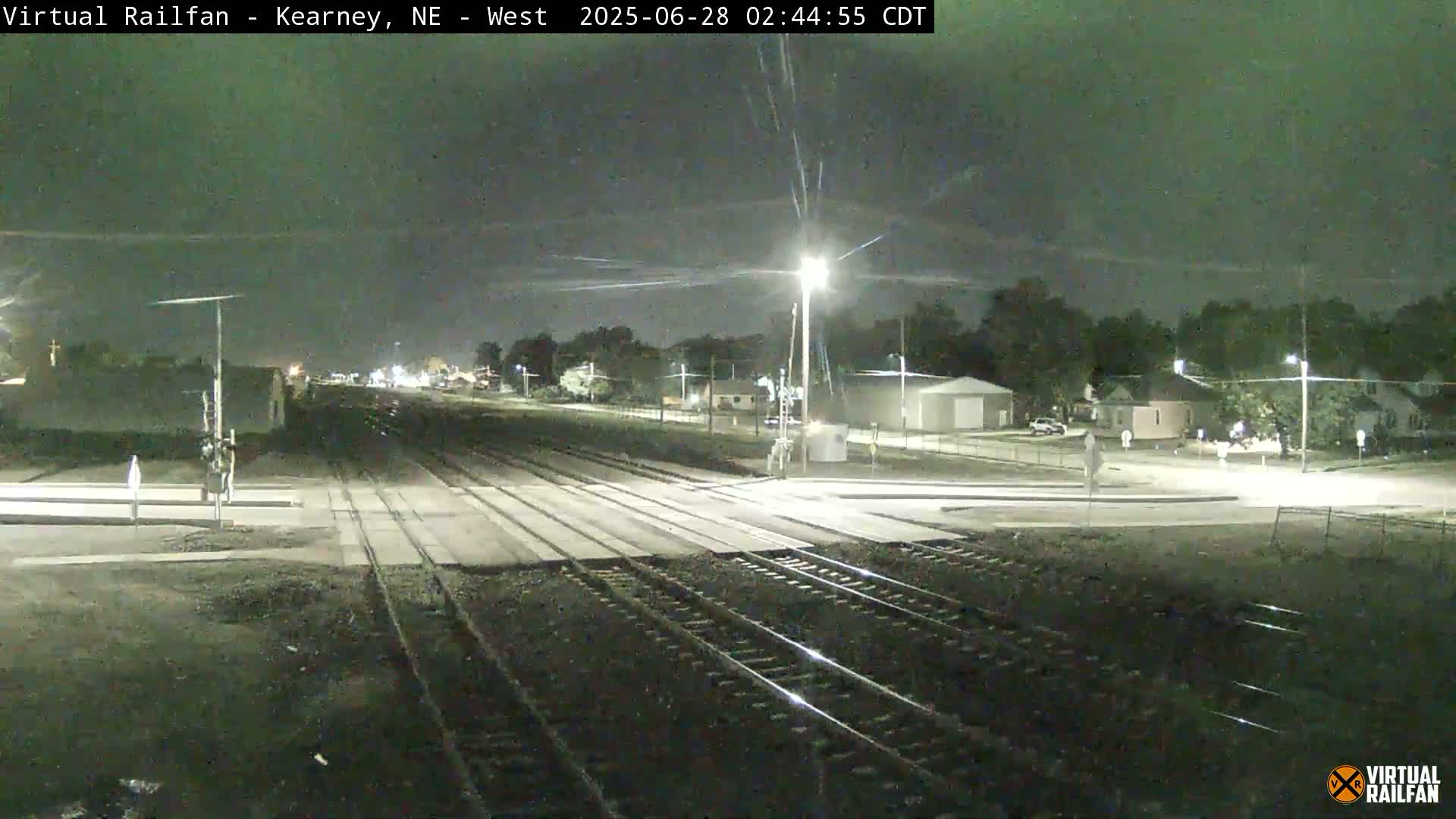 A nighttime view of railroad tracks intersecting with a road, under a dark, clear sky.