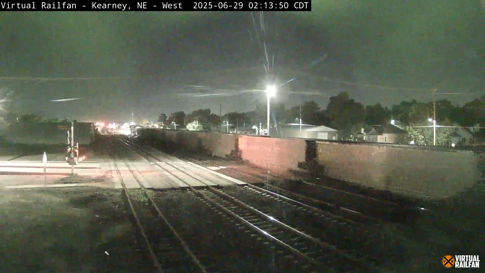 A nighttime view of railroad tracks and a long line of train cars under a dark, possibly slightly overcast sky.