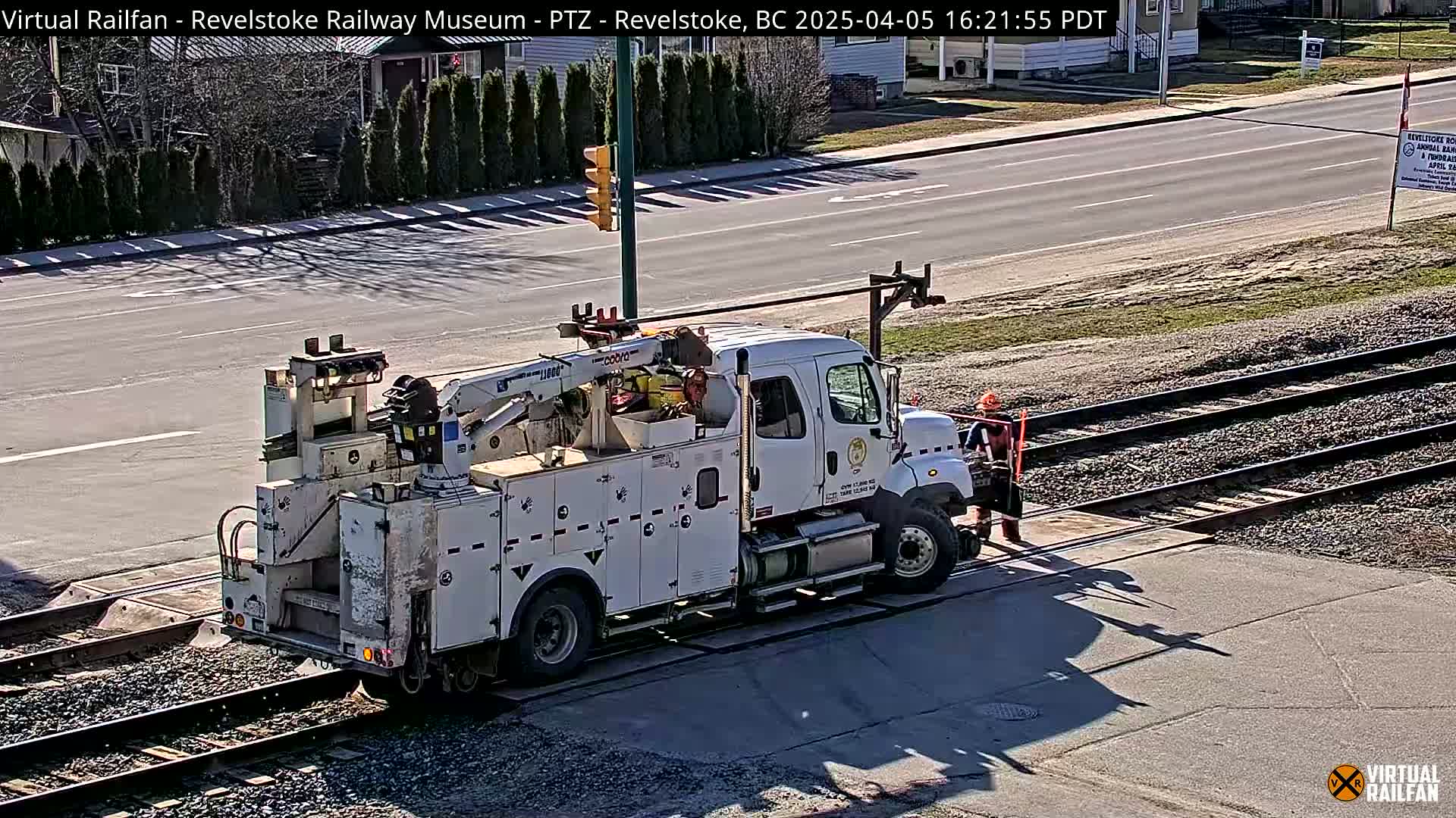 A white utility truck with a crane is parked next to railroad tracks on a sunny day.