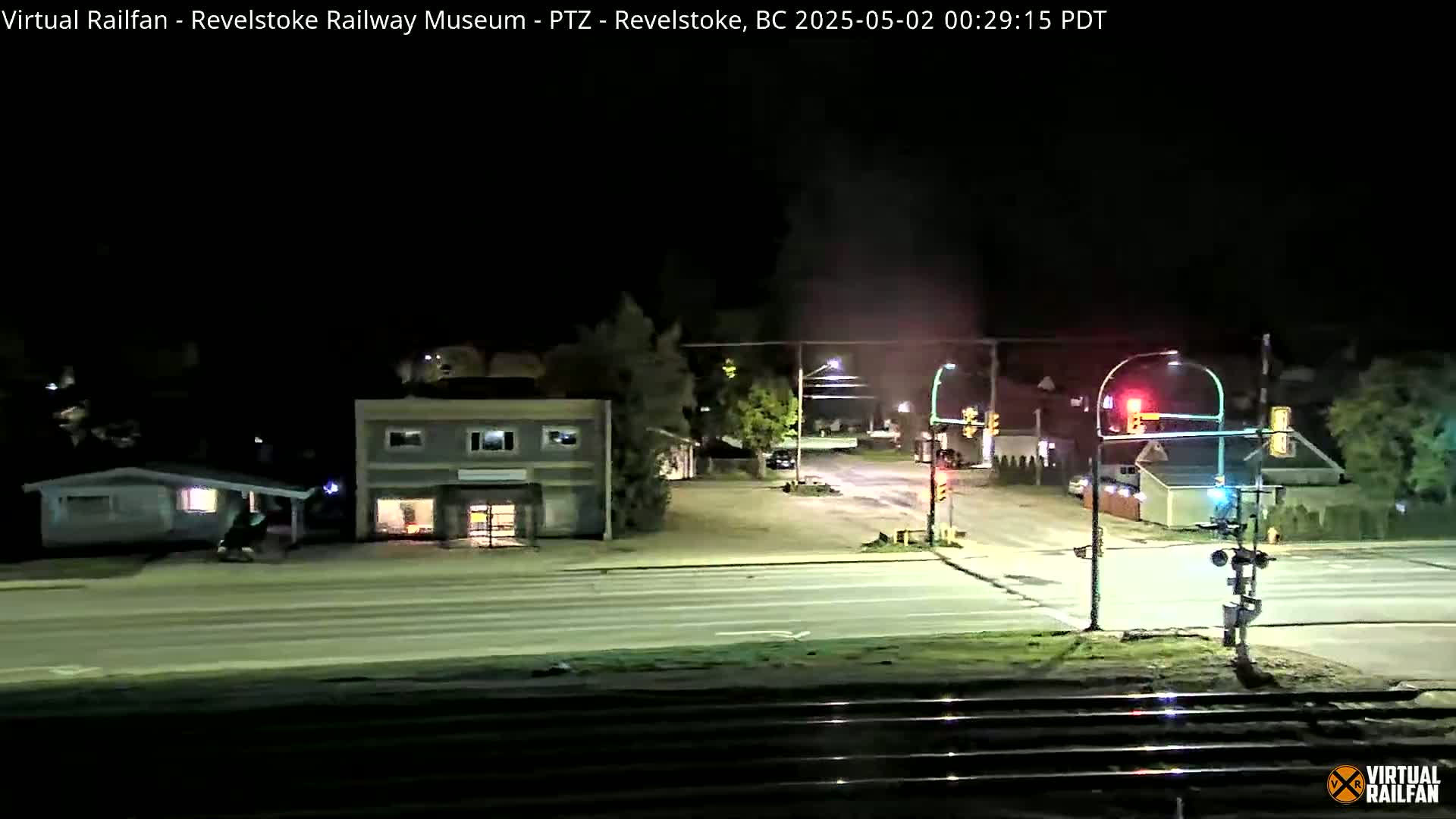 A nighttime view of a quiet intersection with a few buildings and a railway track in the foreground.