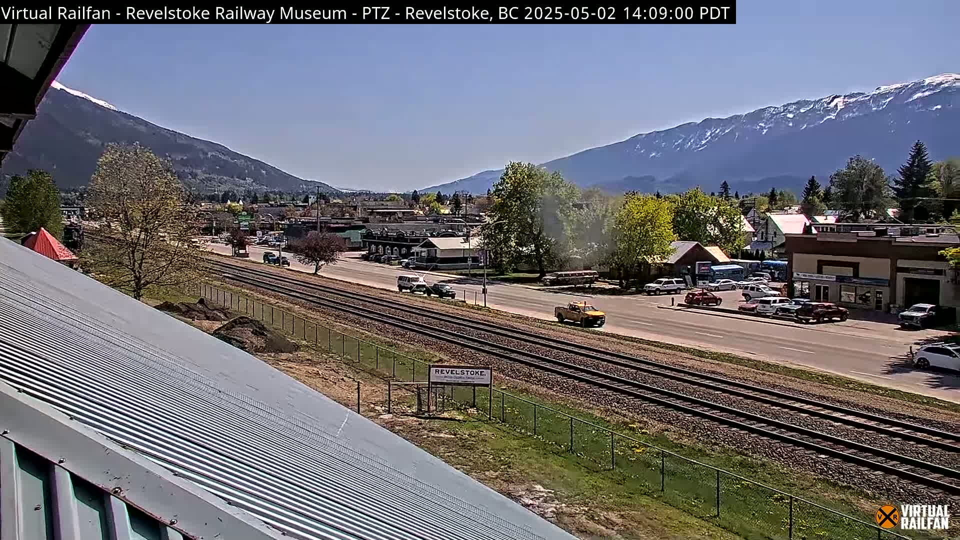 A sunny view of a town beside railroad tracks, with mountains in the background.