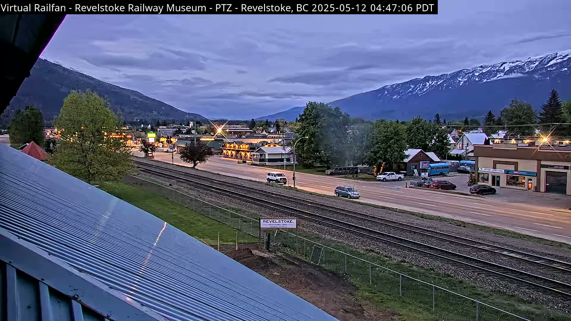 A twilight view of a town nestled in a valley, with mountains in the background and train tracks running through the center of the road.