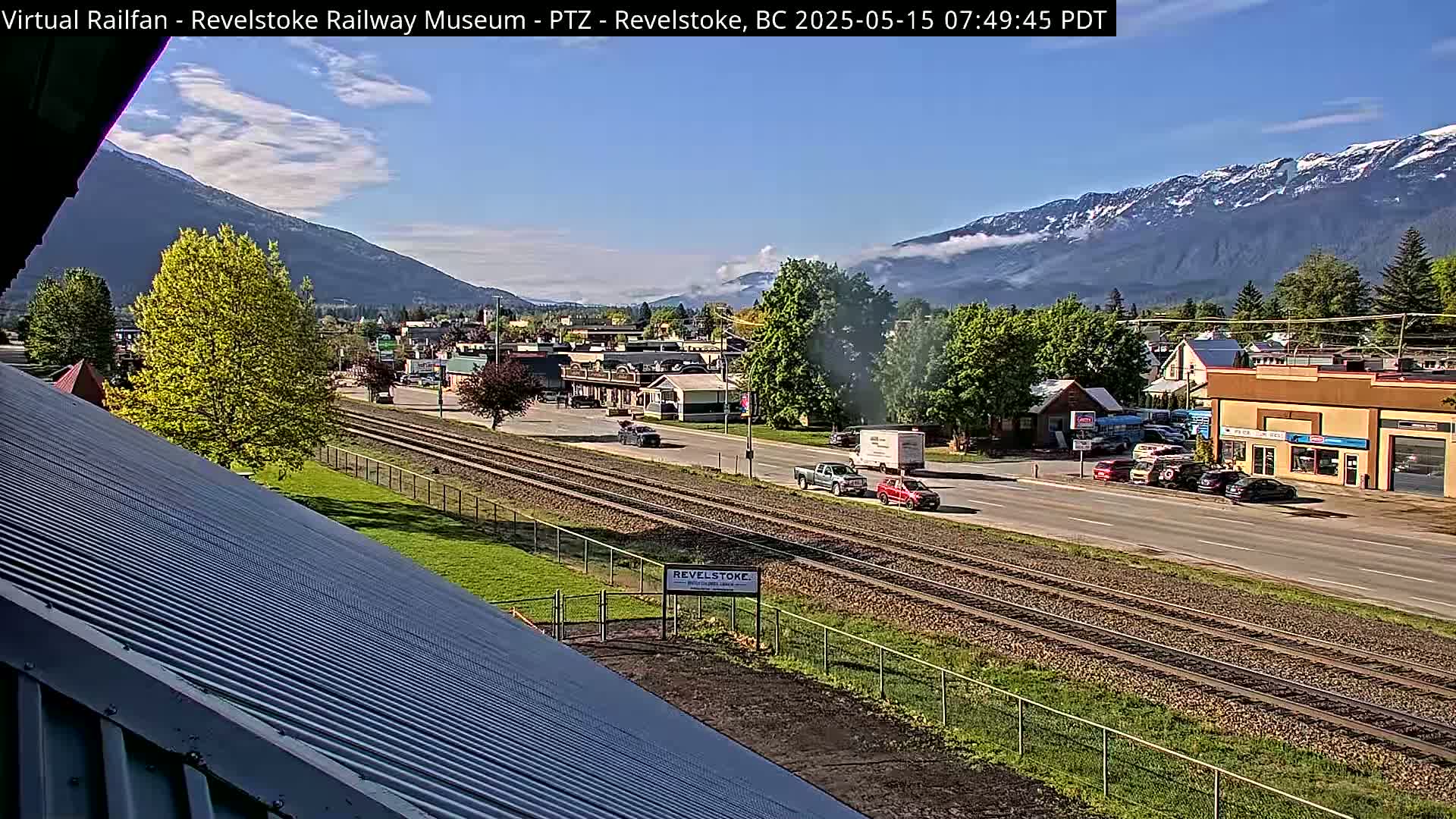 A partly sunny view of a town situated beside train tracks, with mountains in the background.