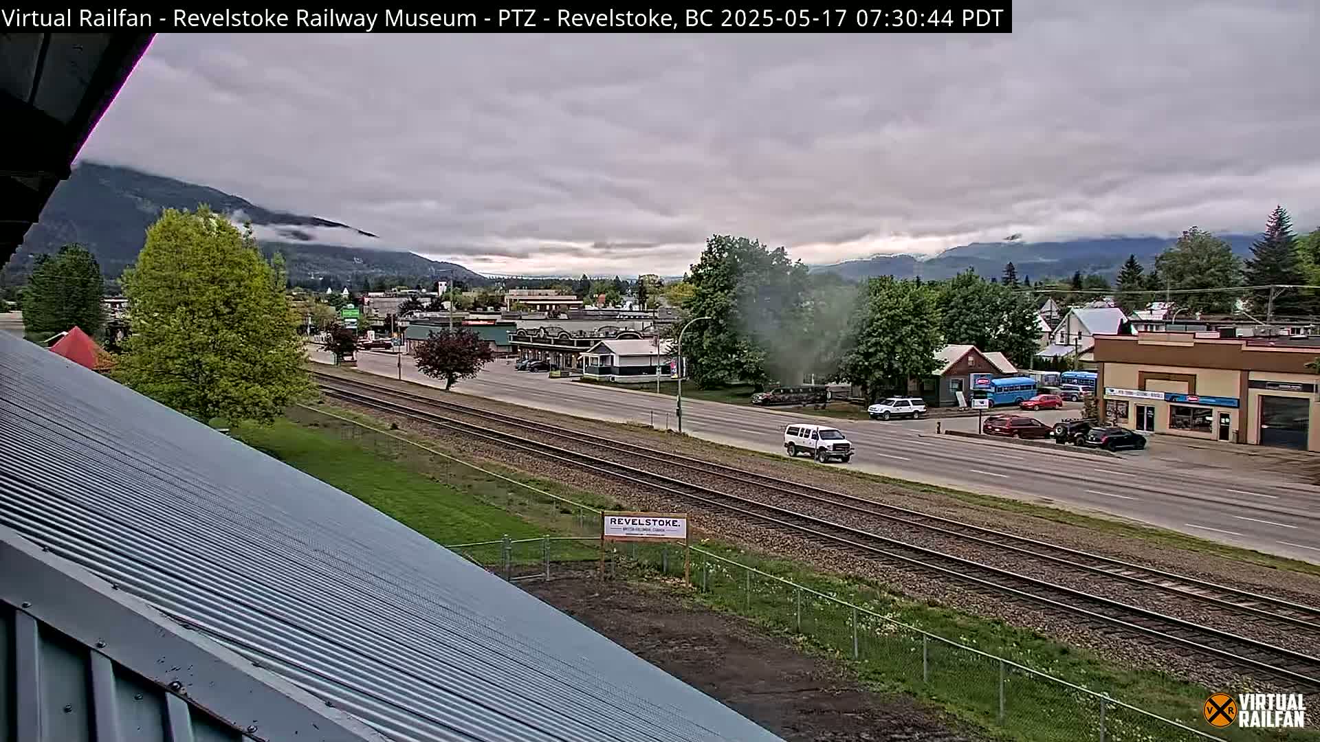 A view of a town beside train tracks under an overcast sky, with mountains in the background.