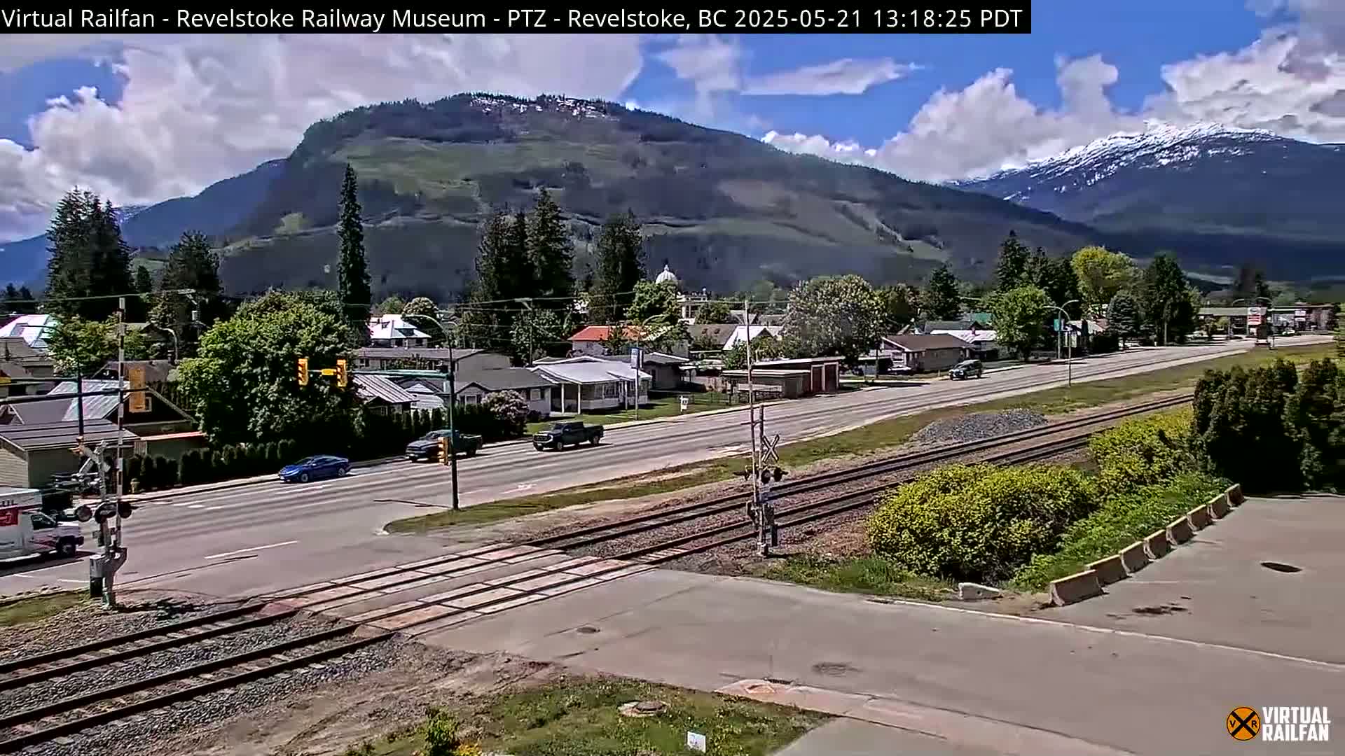 A partly sunny day reveals a town nestled in a valley between mountains, with railroad tracks running through it.