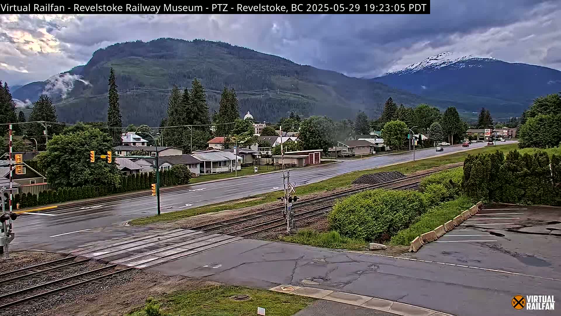 A wet, overcast view of a town nestled in a valley between mountains, showing a road crossing railroad tracks.