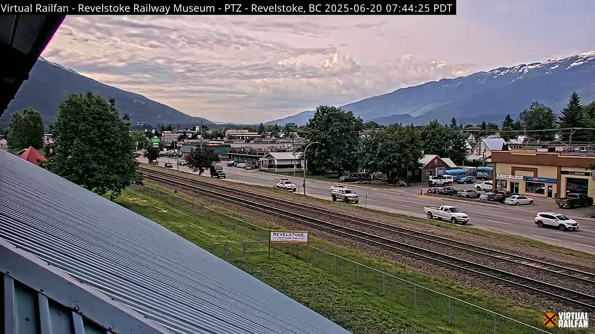 A partly cloudy day reveals a view of a town nestled in a valley between mountains, with railway tracks running through the middle of the town.