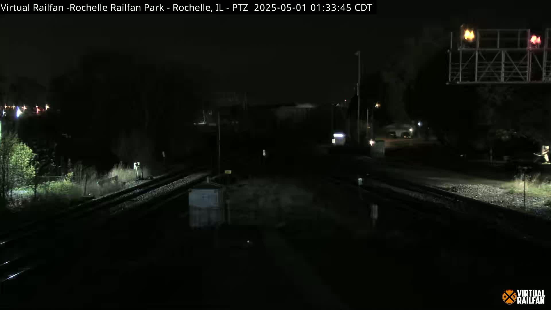 A nighttime view of railroad tracks and surrounding dark areas, illuminated by artificial lights.