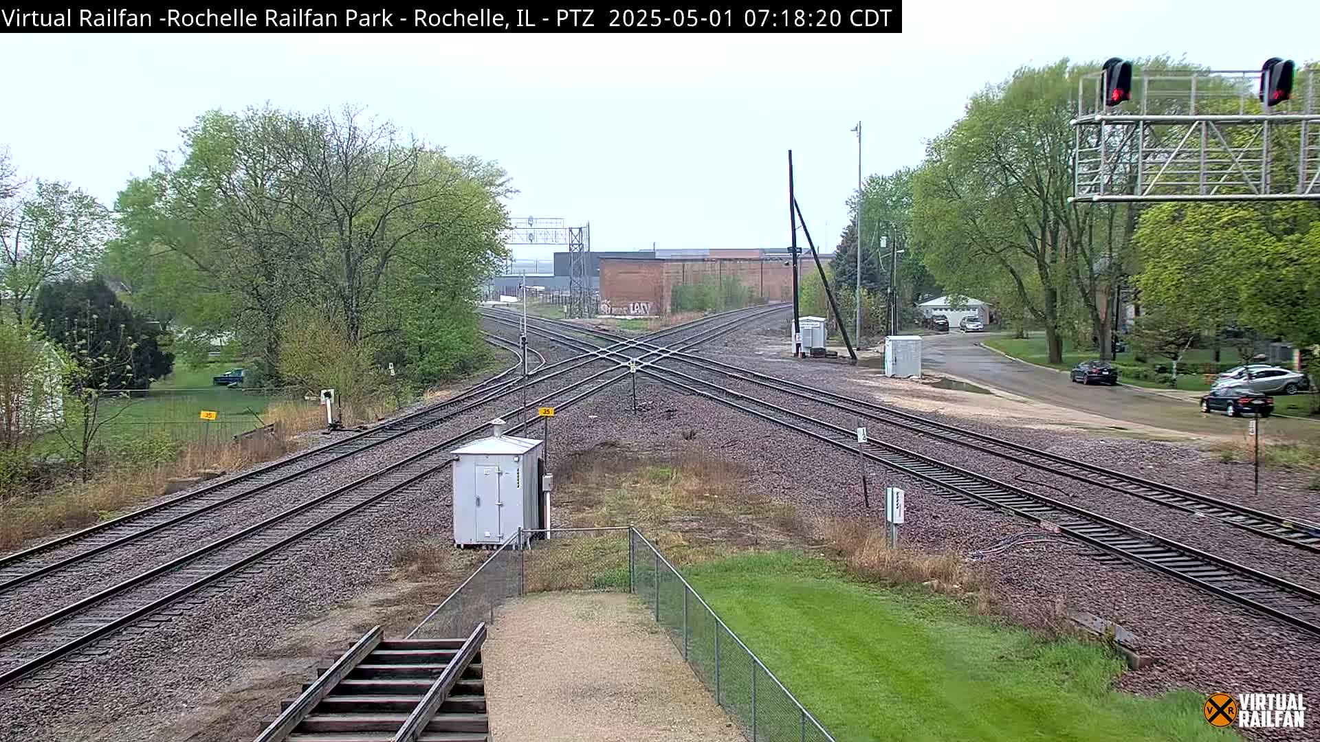 A railroad crossing with several tracks, a small building, and trees under an overcast sky.