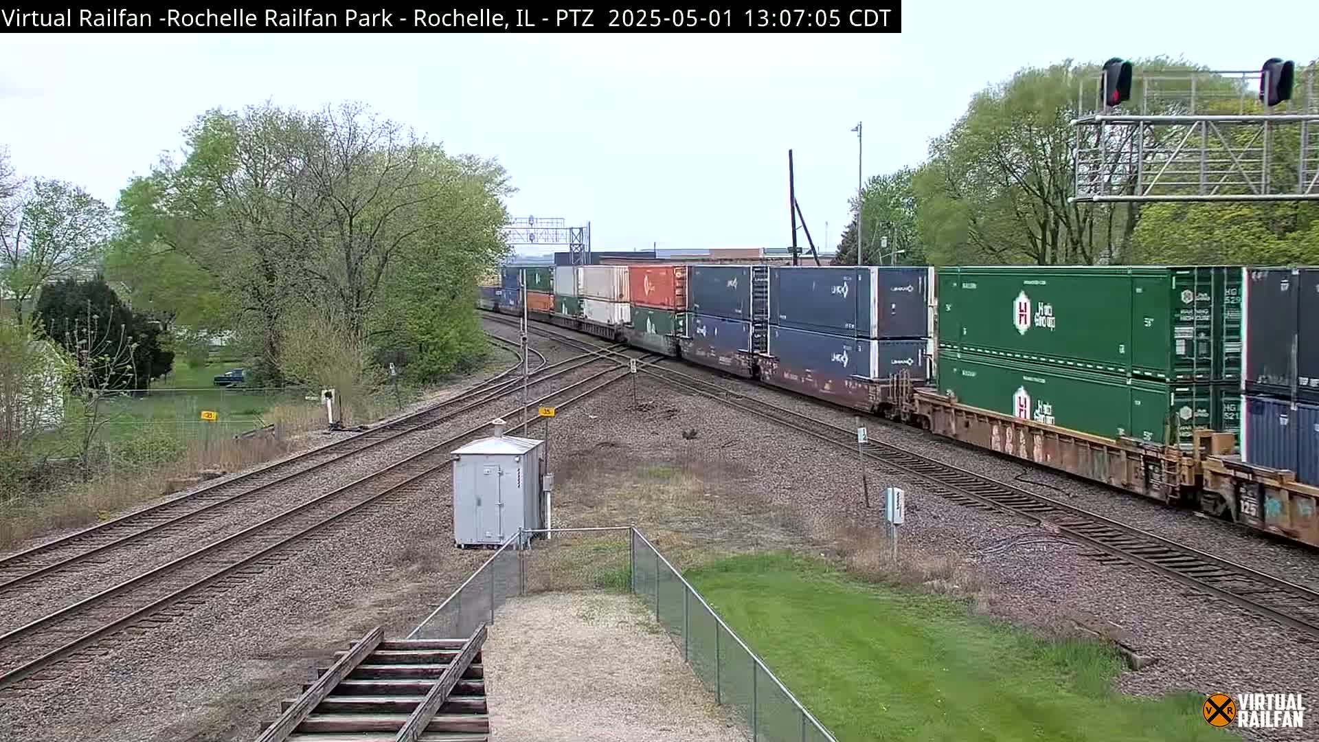 A long freight train carrying numerous shipping containers passes through a railway junction on a partly cloudy day.