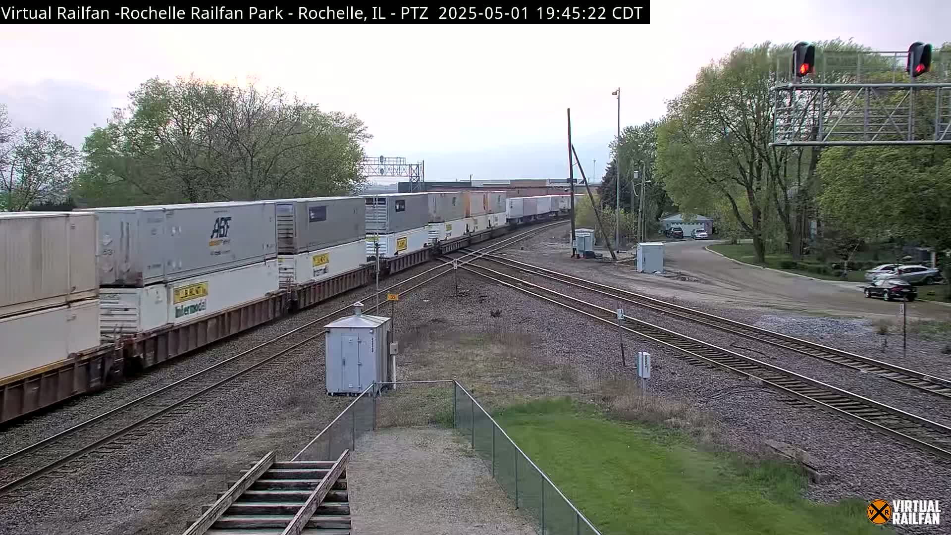 A long freight train carrying multiple shipping containers passes through a railway junction under an overcast sky.