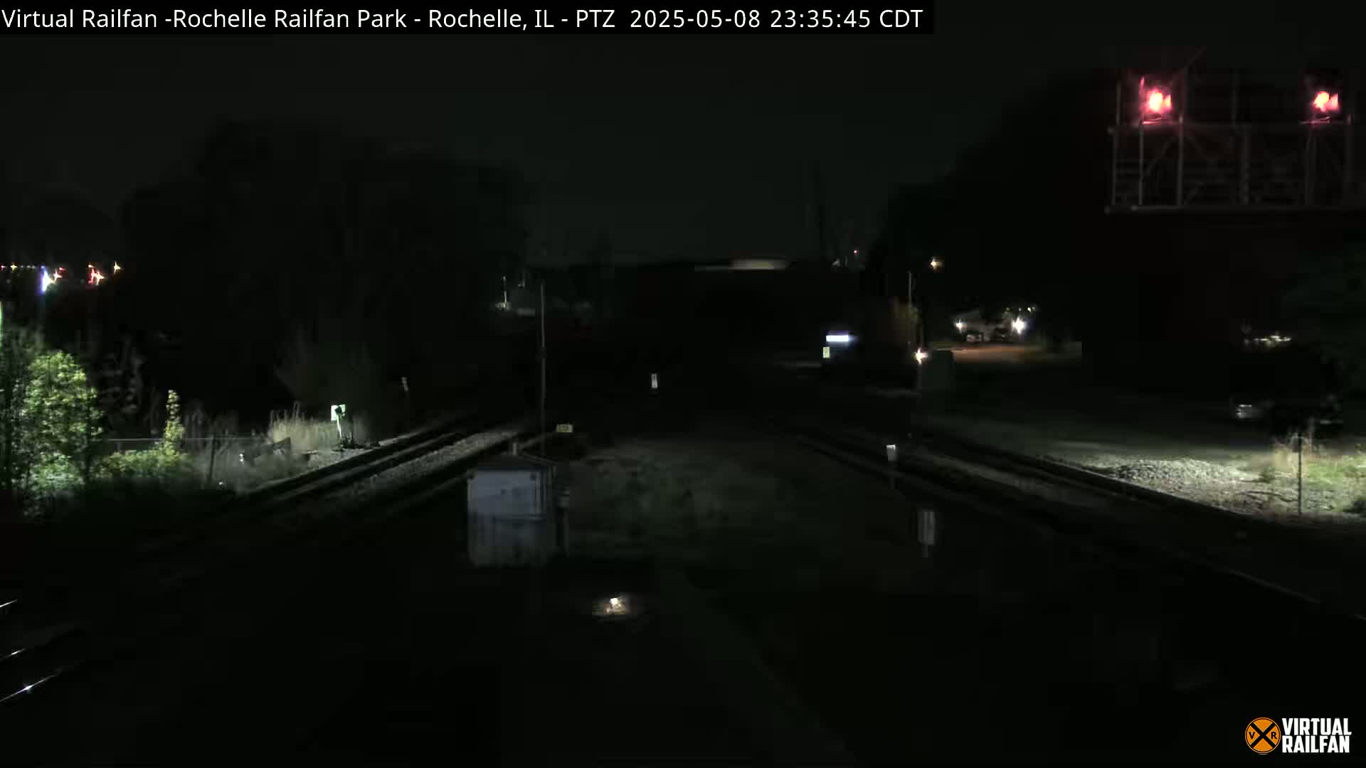 A nighttime view of railroad tracks and surrounding dark, sparsely lit landscape.