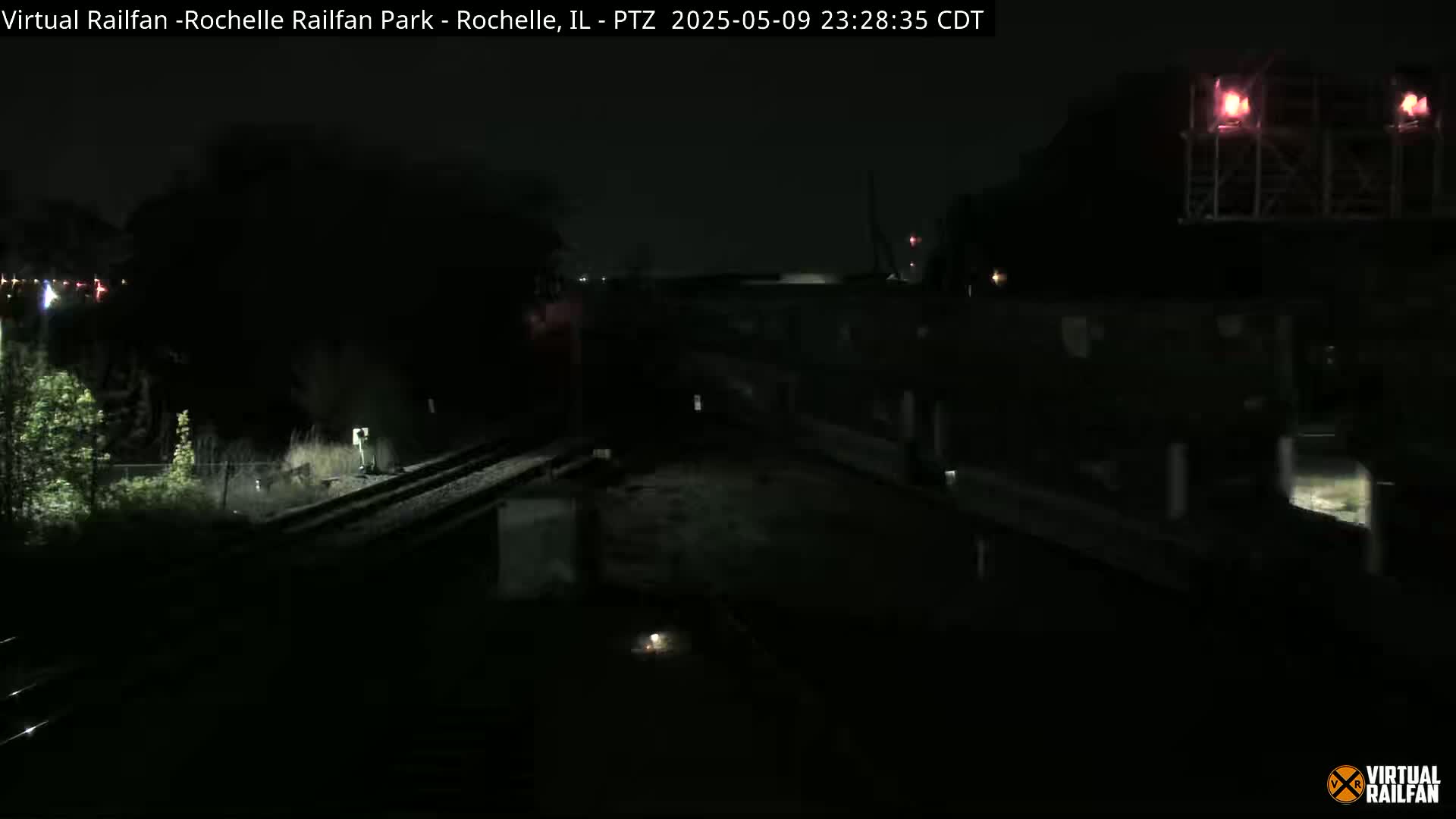 A dark nighttime scene shows a train crossing a set of tracks near a building.