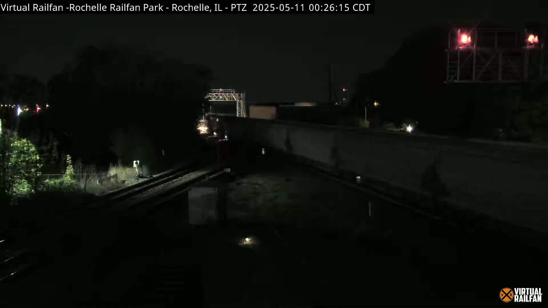 A nighttime view of a train passing by a rail yard under dark, clear skies.