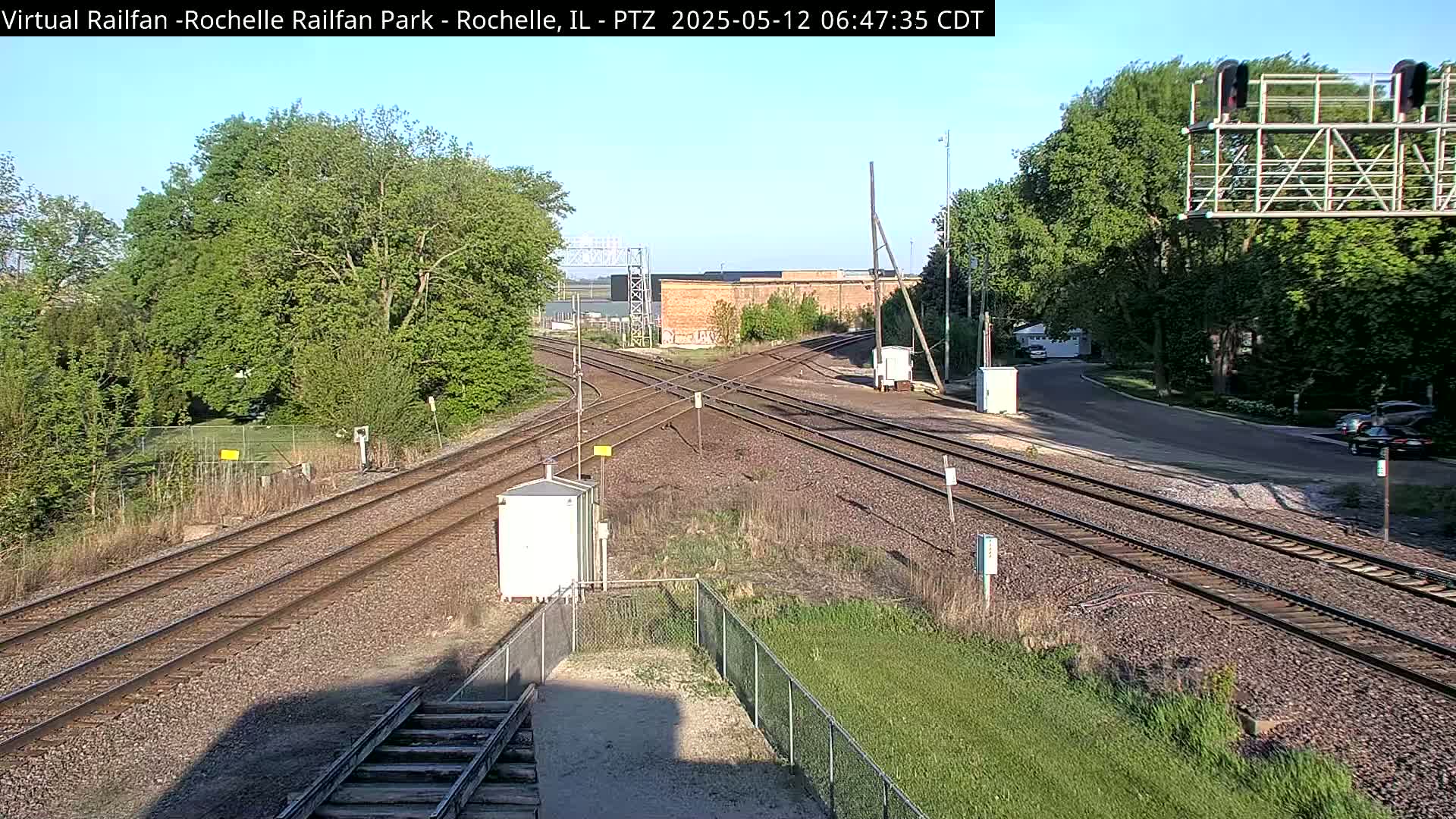 A sunny view of a railway crossing with several train tracks intersecting, surrounded by green trees and vegetation.