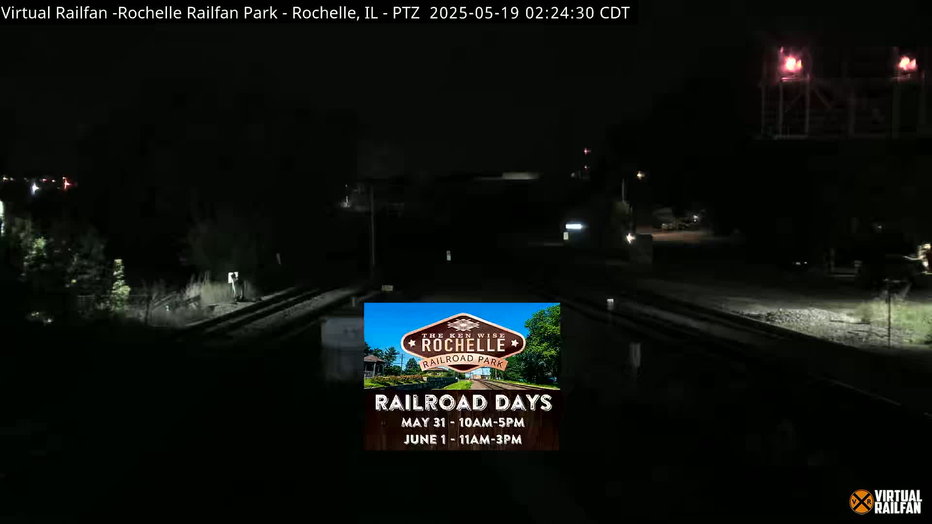 A nighttime view of railroad tracks and a dimly lit area, possibly a railroad park, under dark conditions.