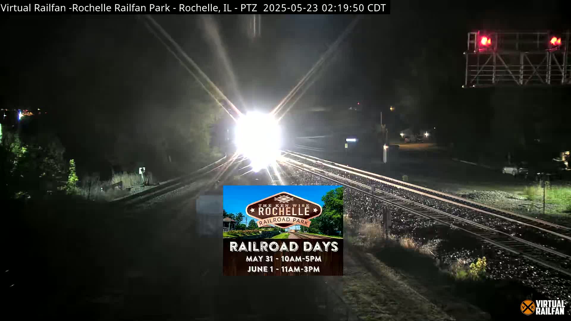 A bright, nighttime train approaches the camera on a set of railroad tracks.