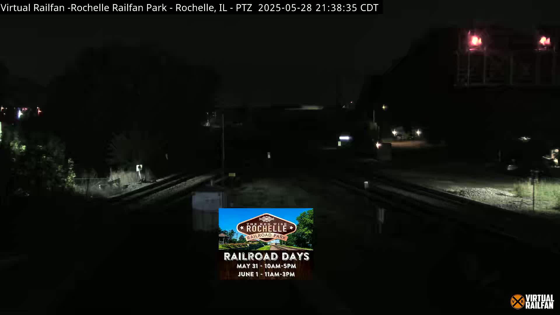 A nighttime view of railroad tracks and a dark building under a clear, dark sky.