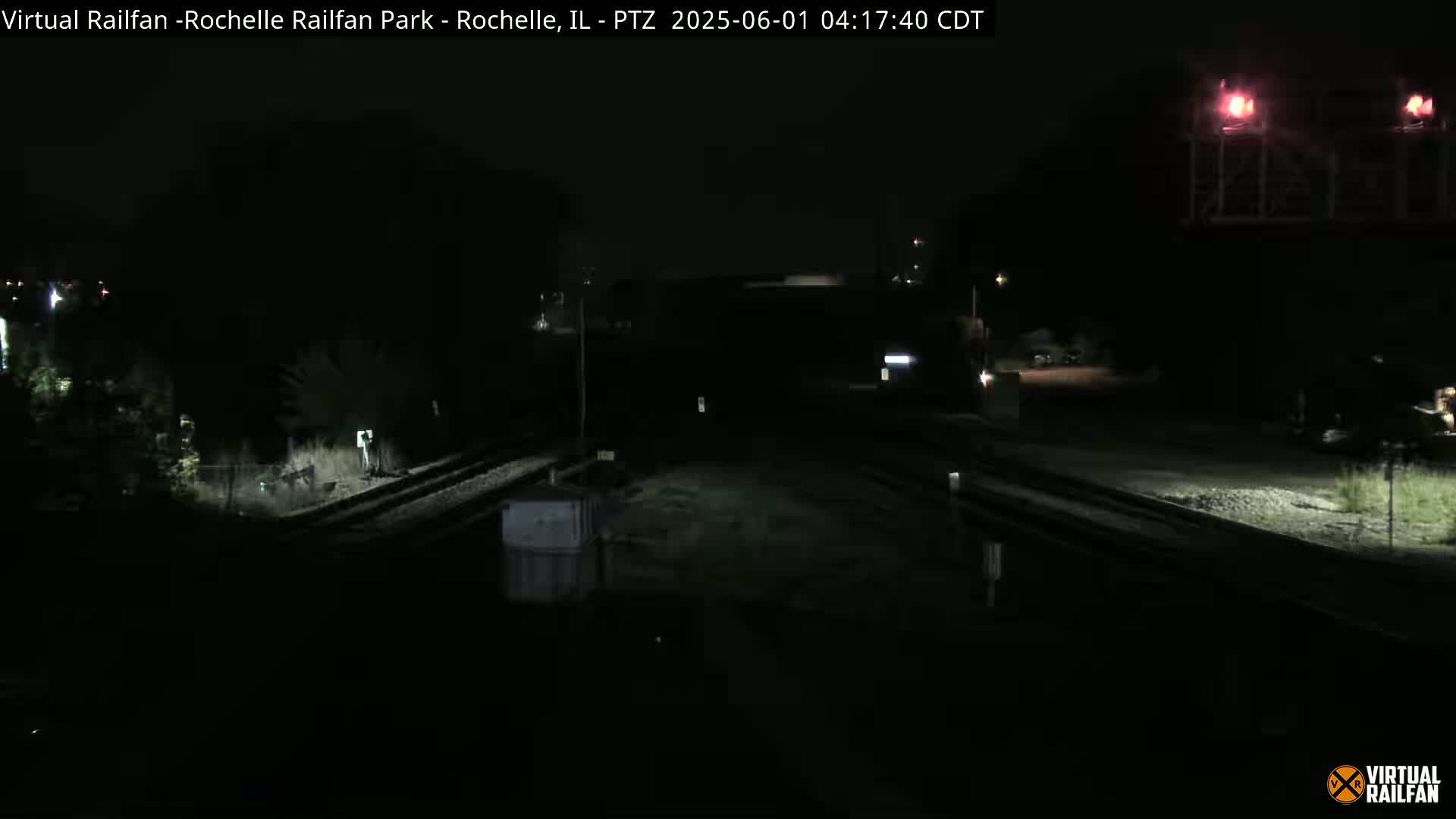 A nighttime view of railroad tracks and a dark, wet area, illuminated by artificial light.