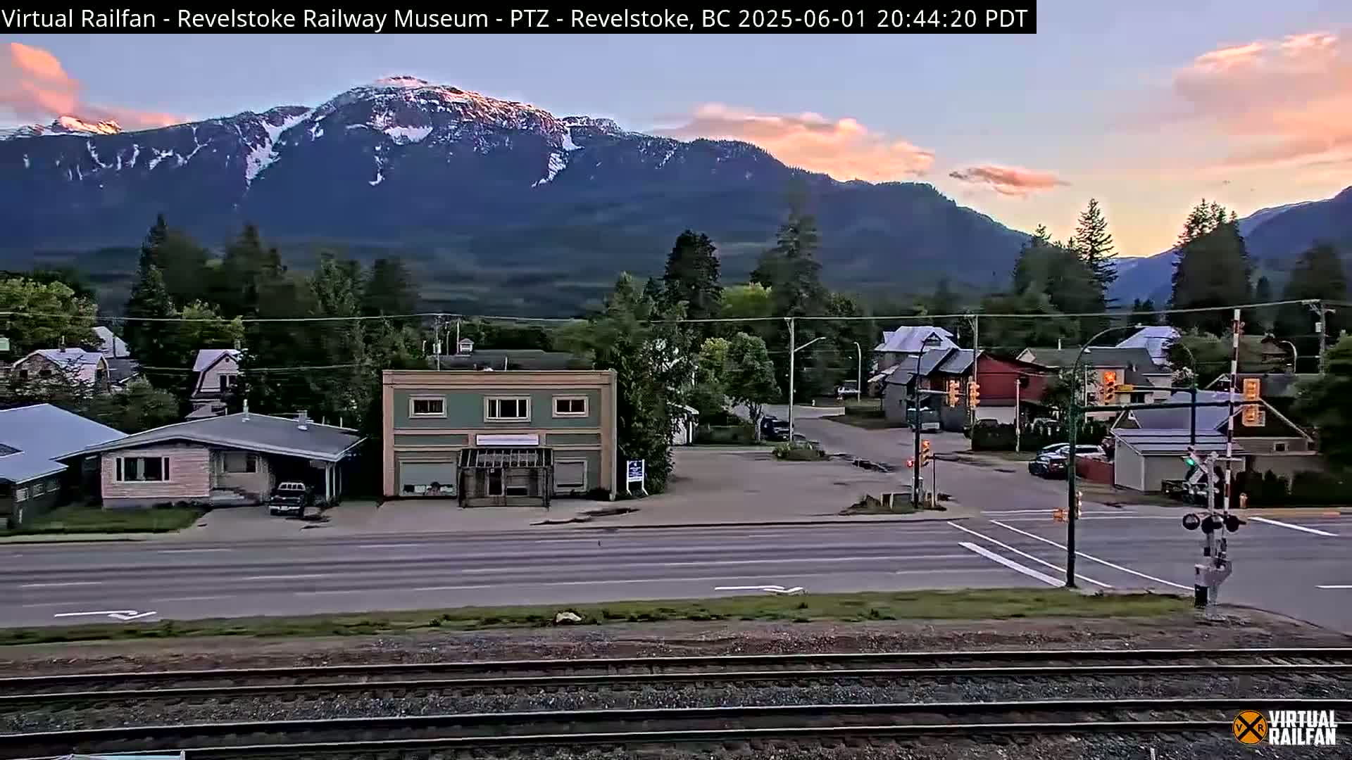 A small town nestled in a valley, overlooked by snow-capped mountains under a twilight sky.