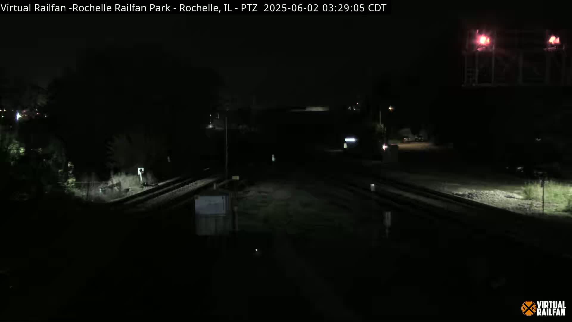 A nighttime, dark view of railroad tracks and a nearby road, with minimal ambient light.