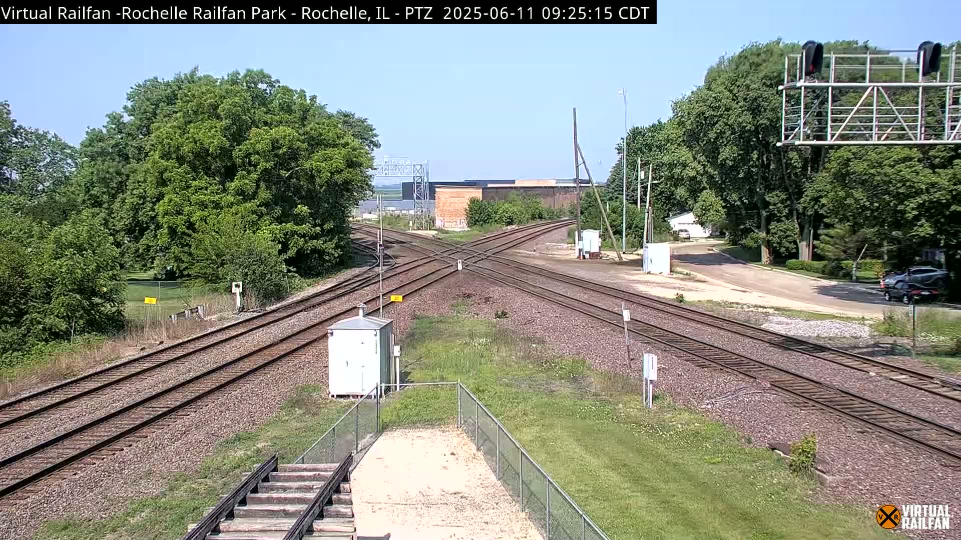 A sunny day reveals a railway crossing with several train tracks intersecting, surrounded by lush green trees and grass.