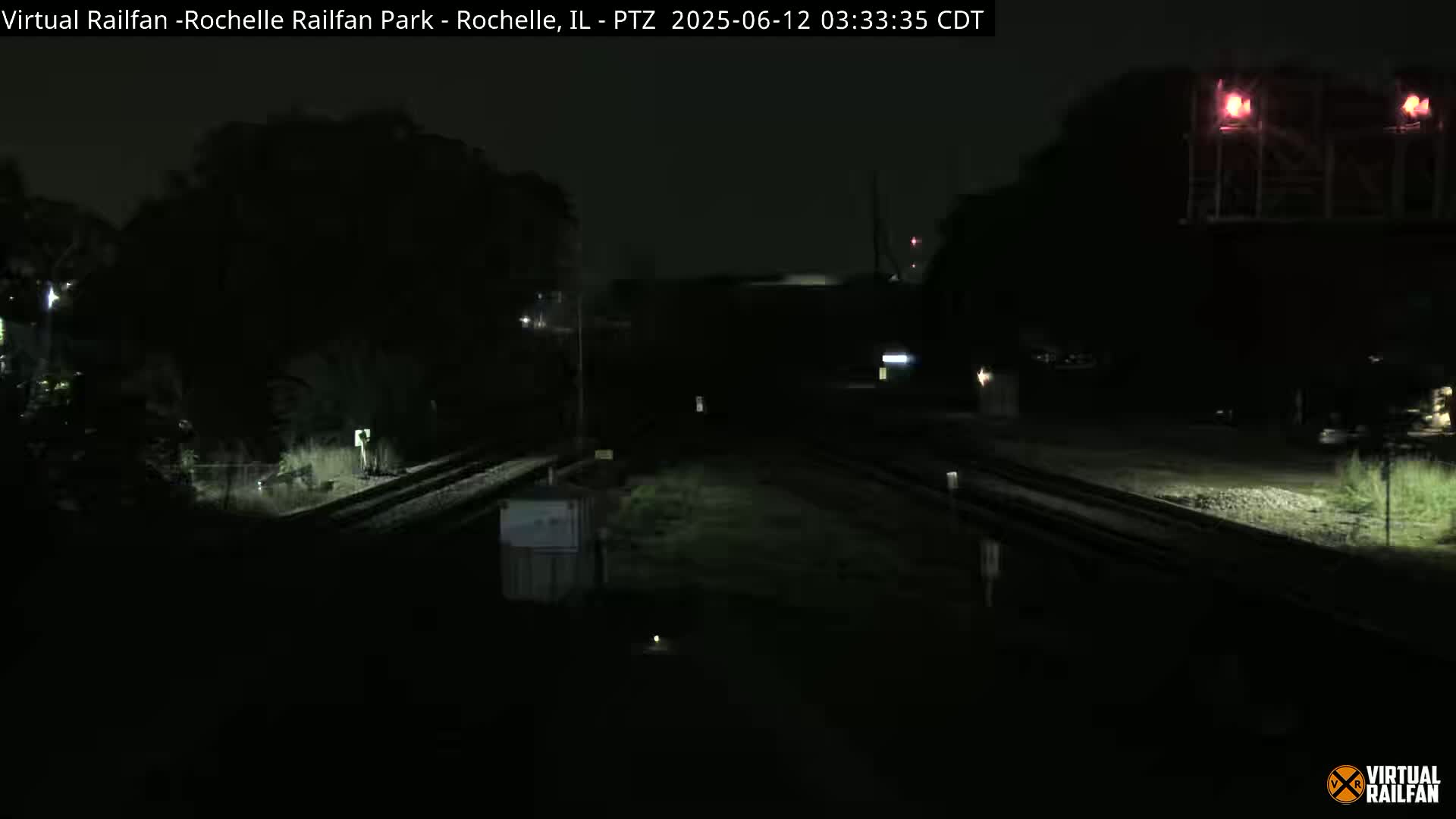 A dark nighttime view of a train crossing, illuminated by artificial lights.