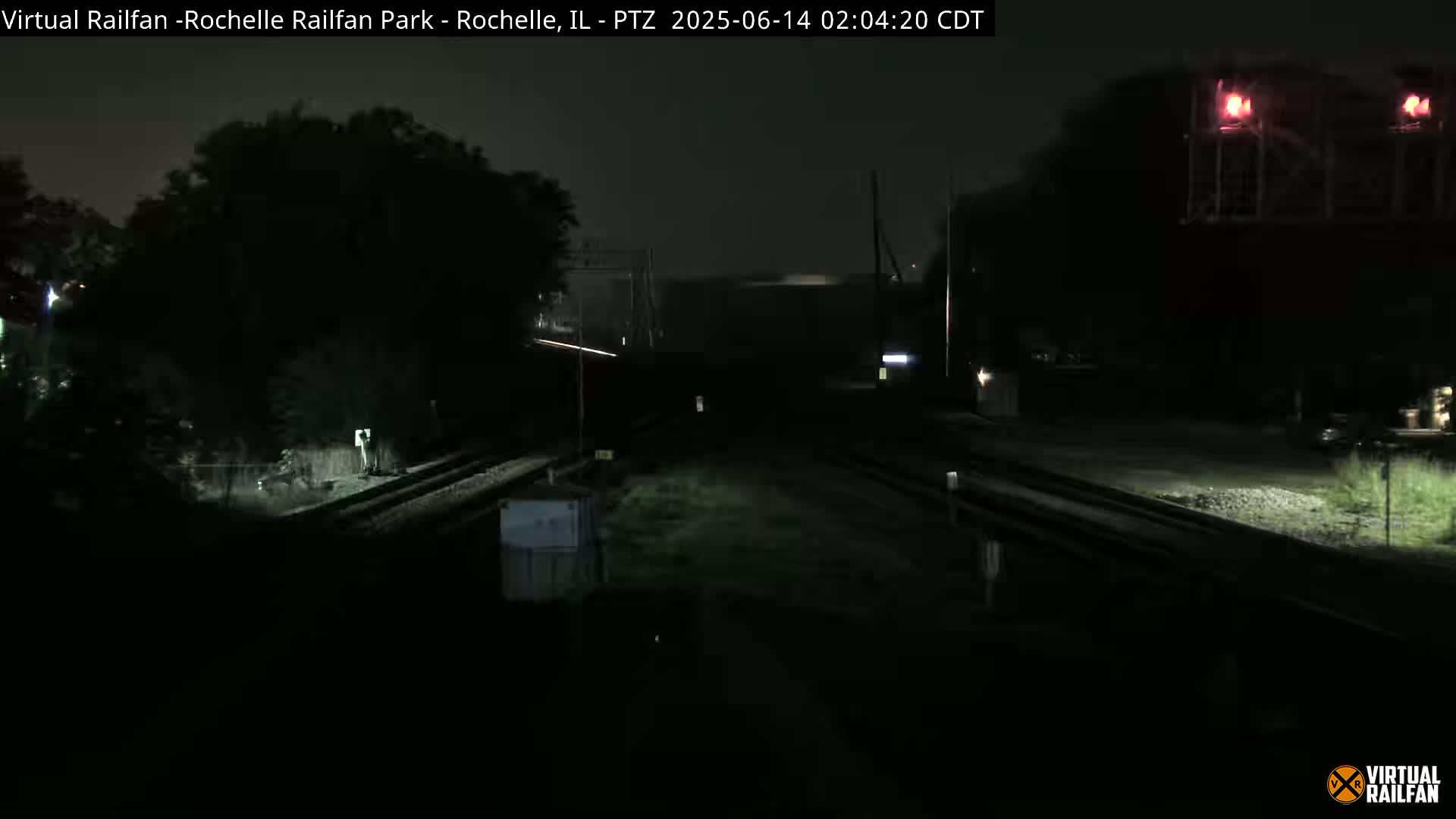 A nighttime view of dark railroad tracks extending into the distance under a cloudy sky.