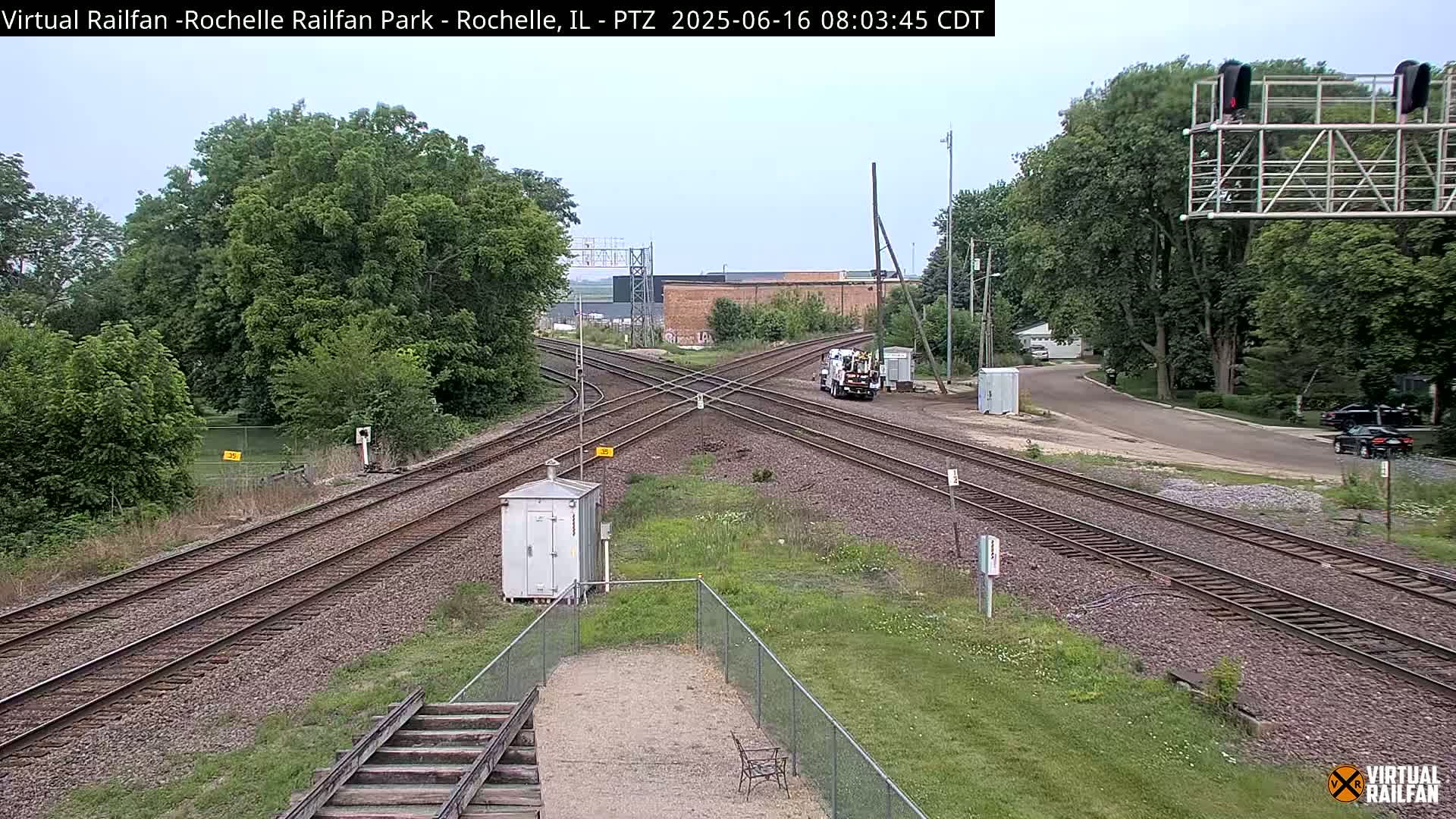 A train crossing with several tracks, surrounded by green grass and trees under an overcast sky.