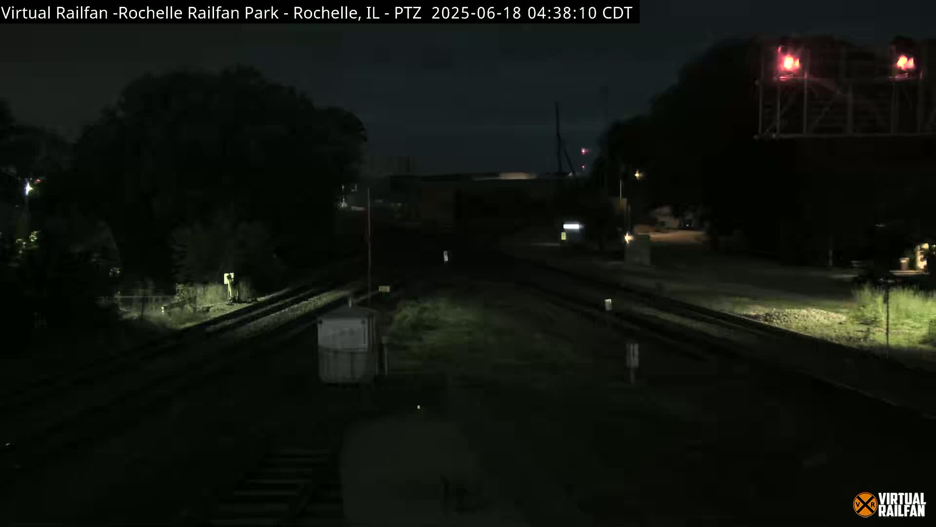 A nighttime view of a dimly lit train track intersection, with some vegetation visible on either side.