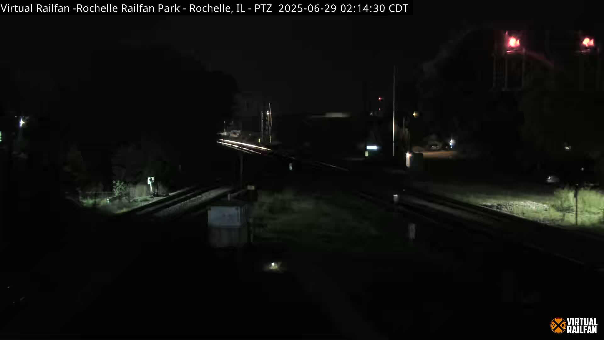A nighttime view of a dimly lit railroad crossing with train tracks and surrounding vegetation.