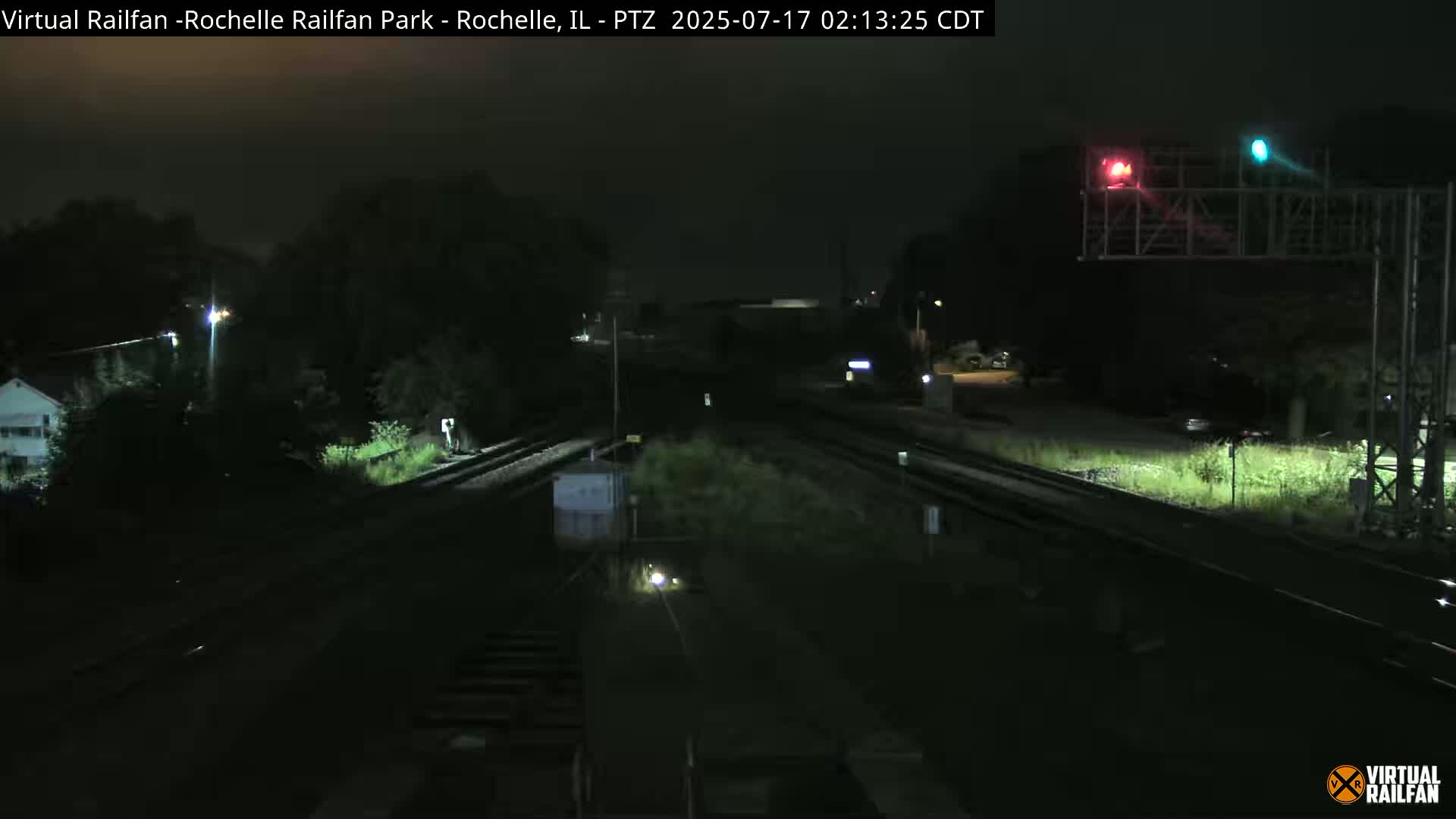 At night, a dark train yard with railroad tracks and signals is dimly lit.