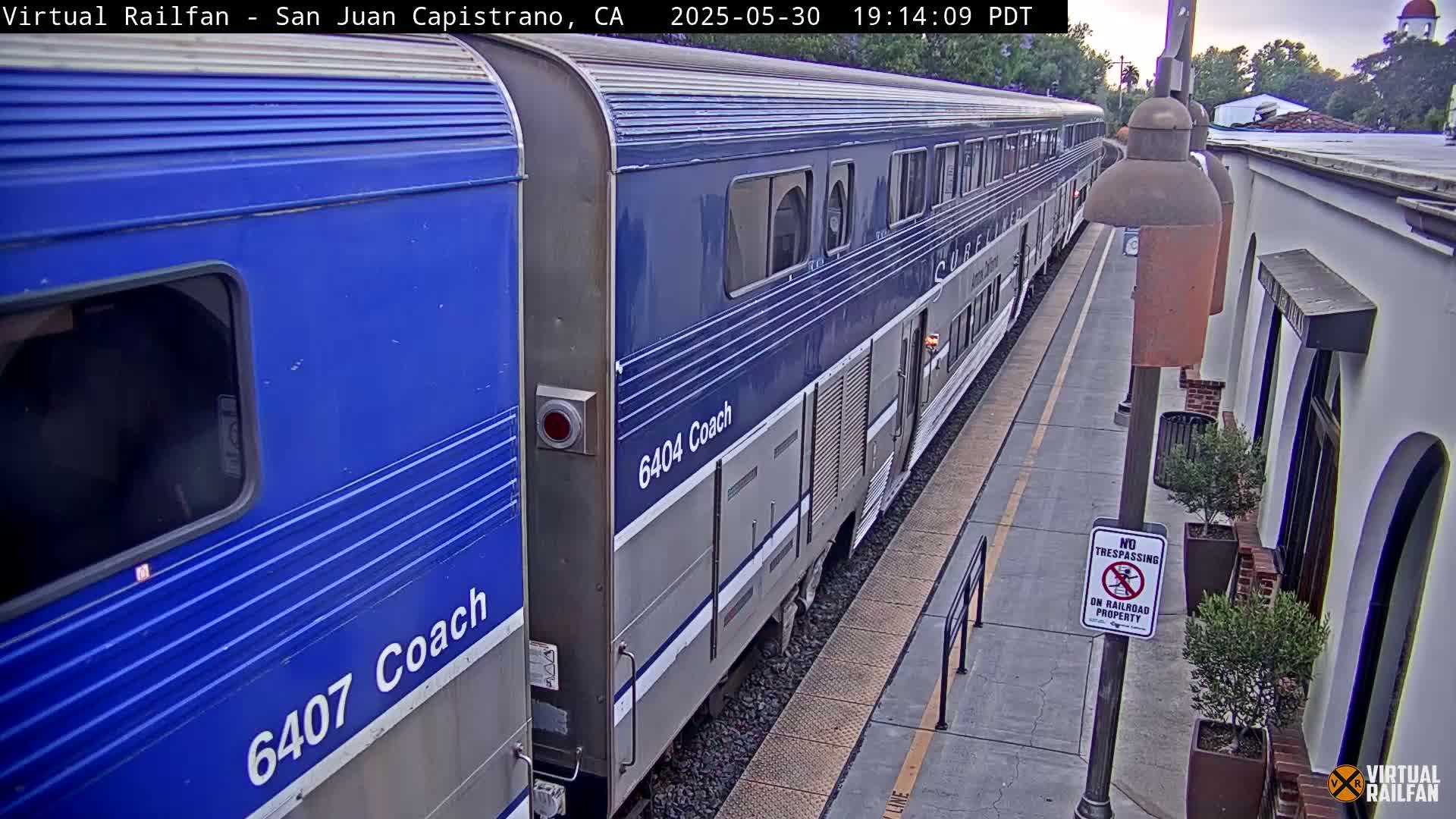 A blue and silver passenger train is stopped at a station platform on an overcast day.