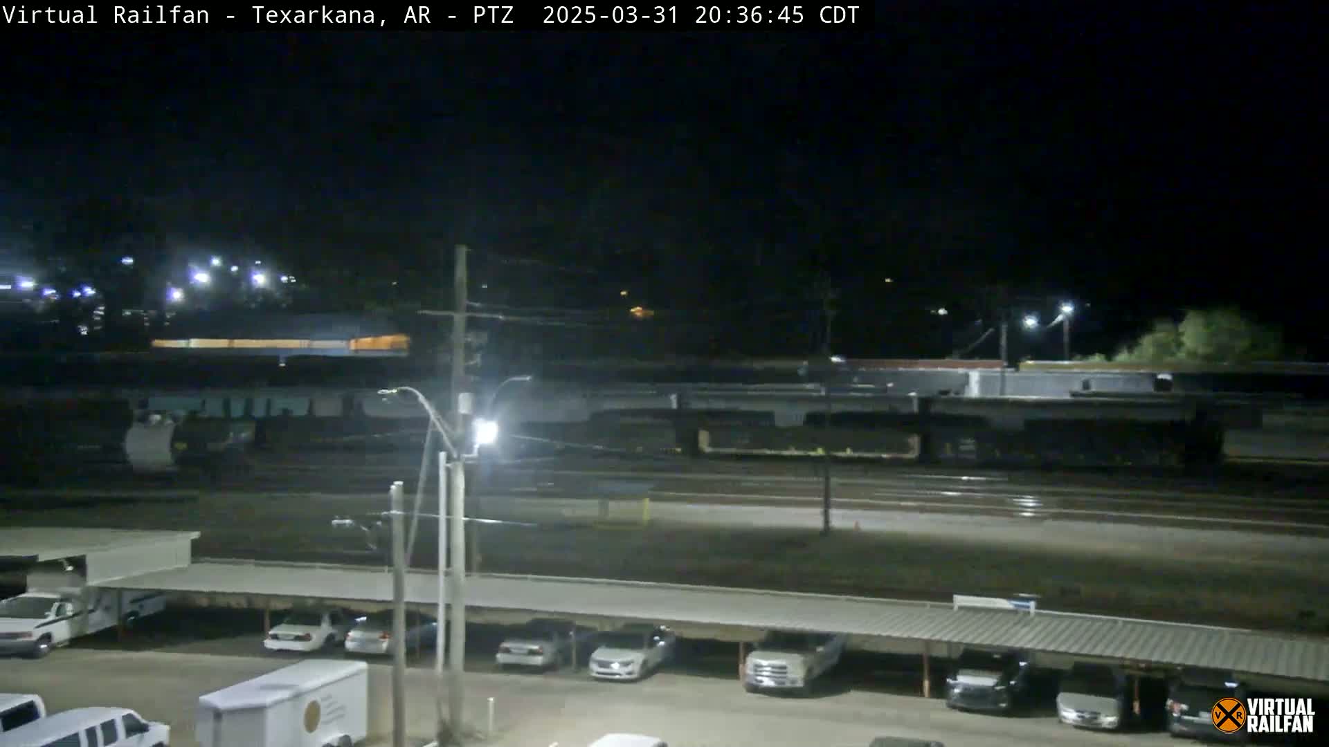 A long freight train passes by a parking lot at night under dark, clear skies.